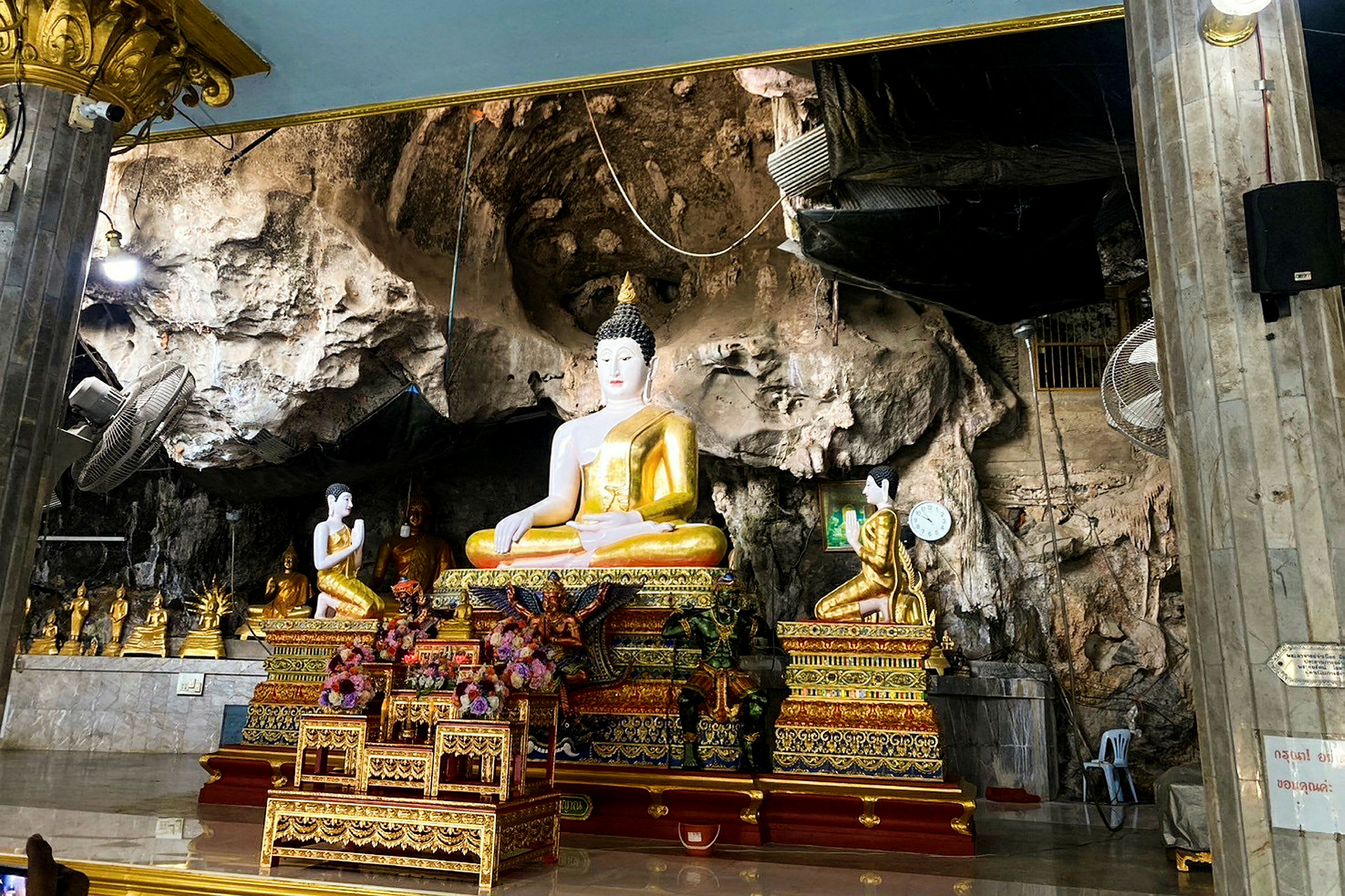Billedet viser en buddhastatue i et dekoreret miljø med klippevægge. (AI-genereret tekst)