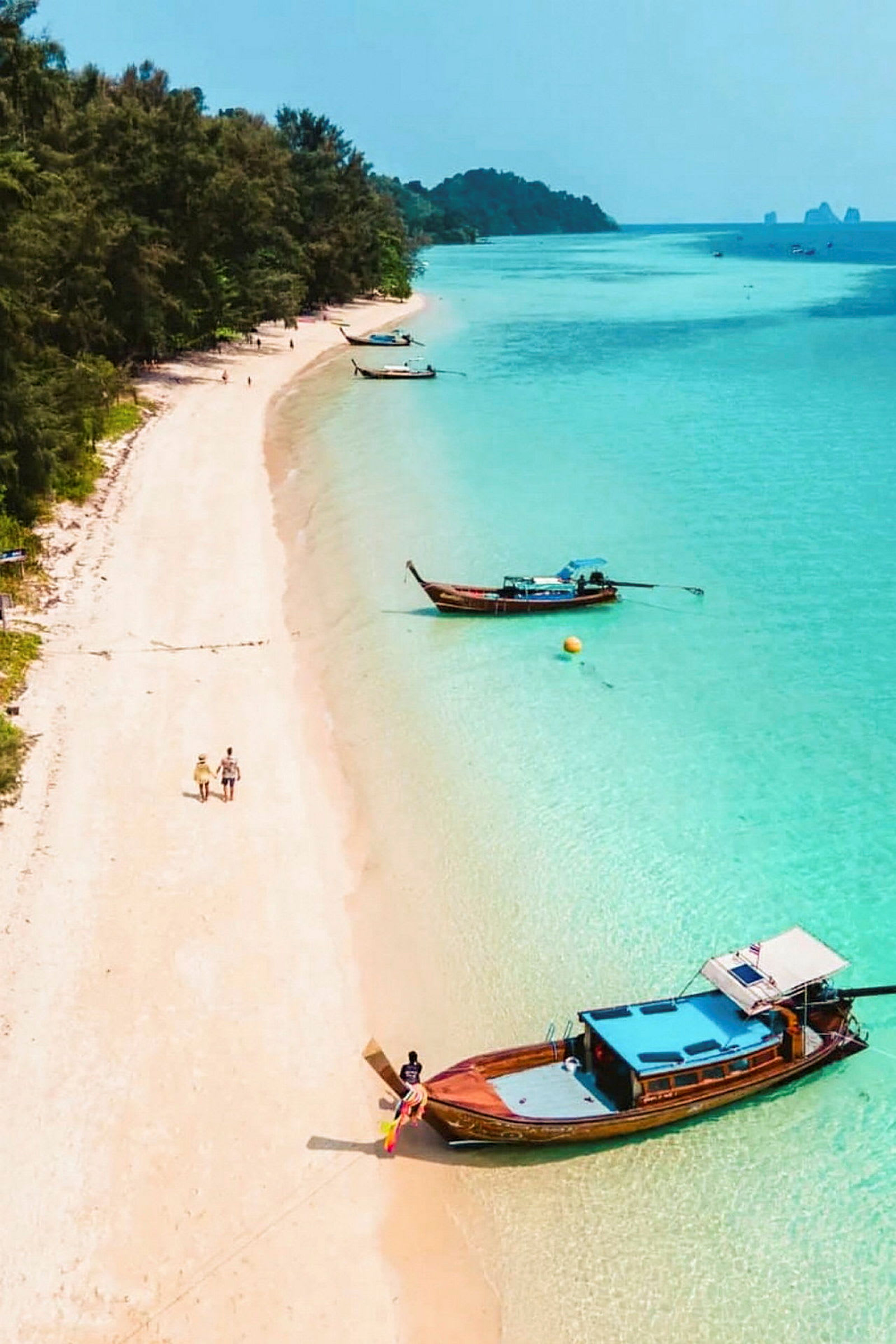 Billedet viser en gylden strand med klart turkis vand og træbåde tæt på kysten. (AI-genereret tekst)