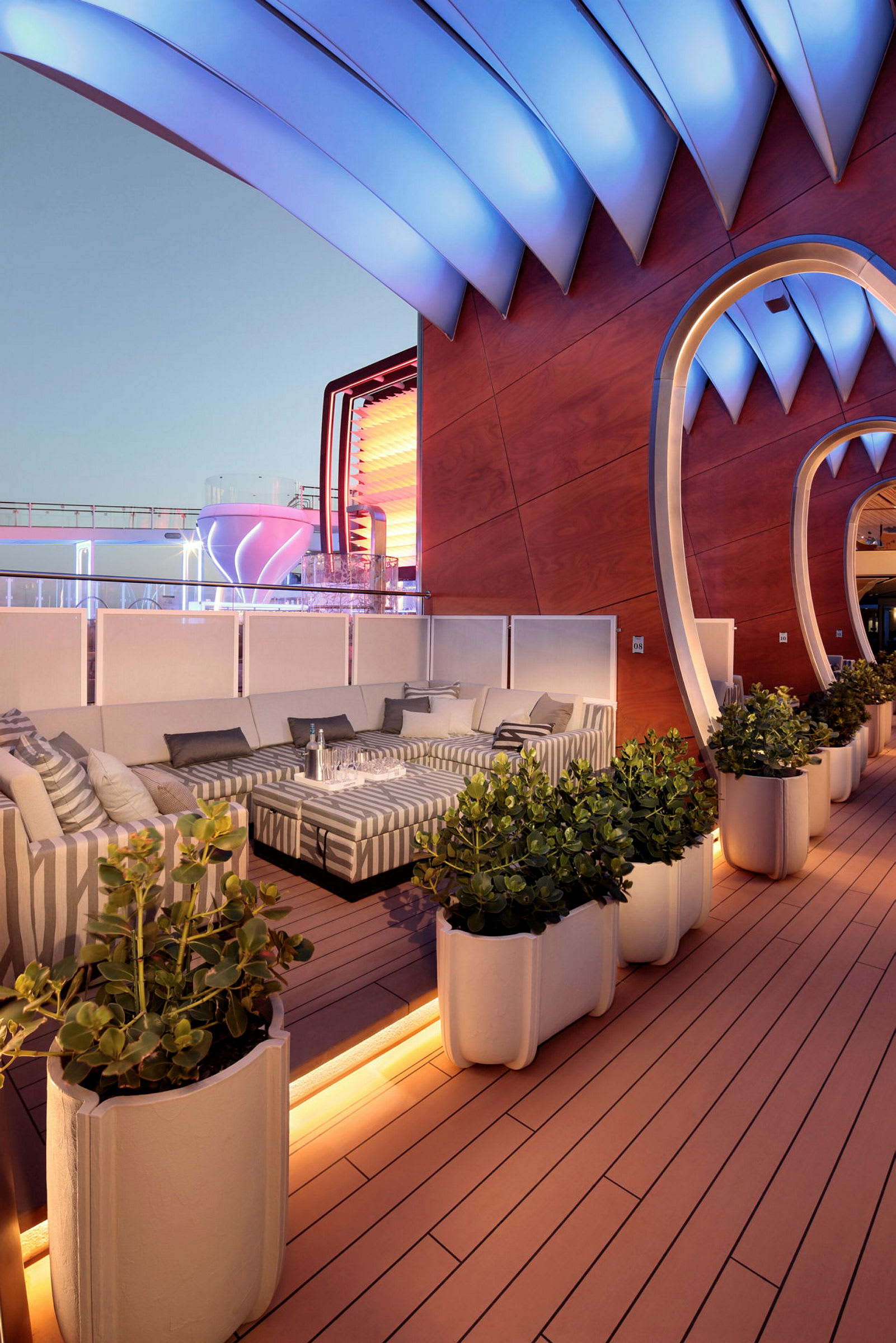 En moderne lounge med sofaer, planter og arkitektoniske detaljer udendørs under aftenbelysning. (AI-genereret tekst)