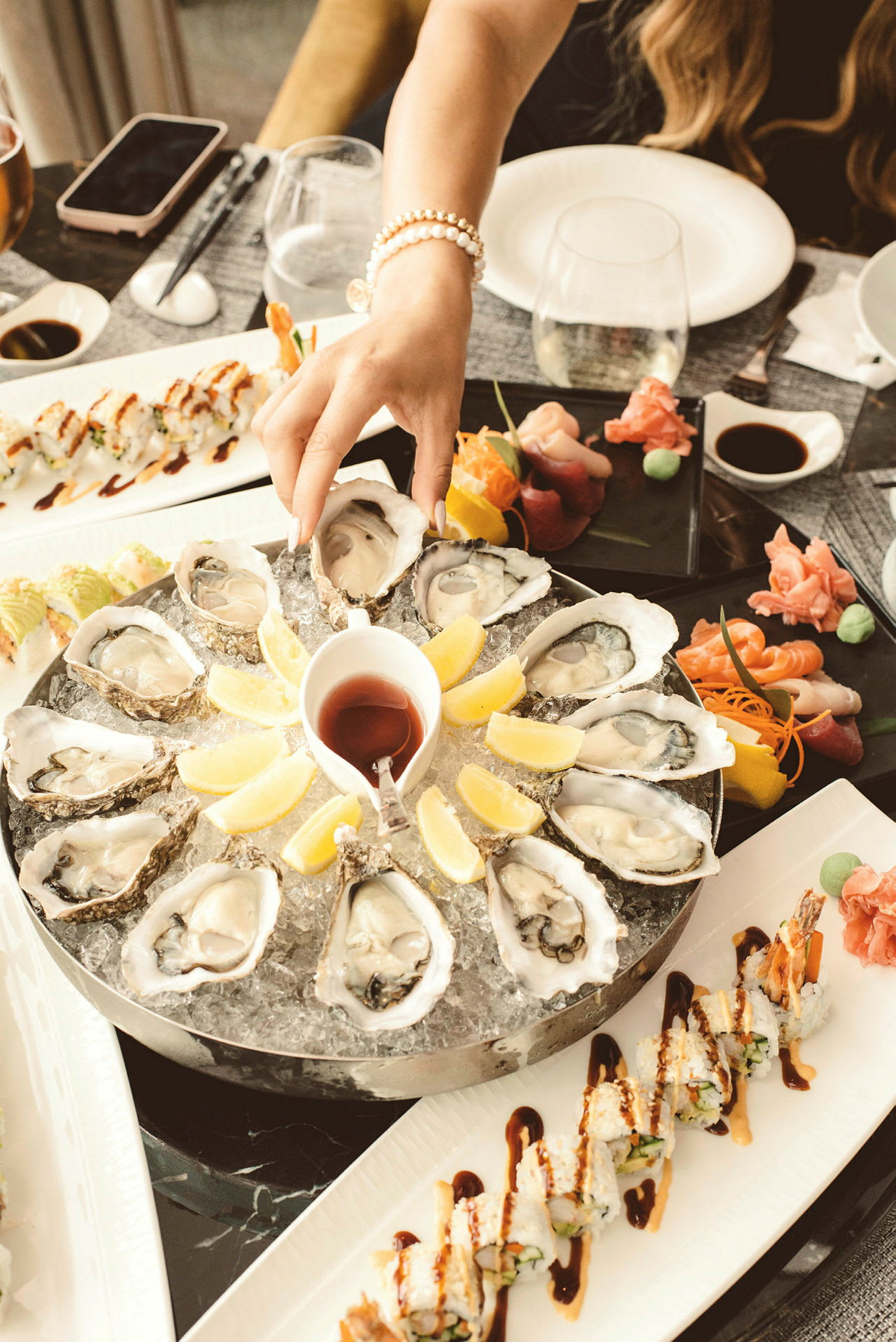 En tallerken med østers serveret på is med citronbåde i midten, sammen med sushi og sashimi på andre tallerkener. (AI-genereret tekst)