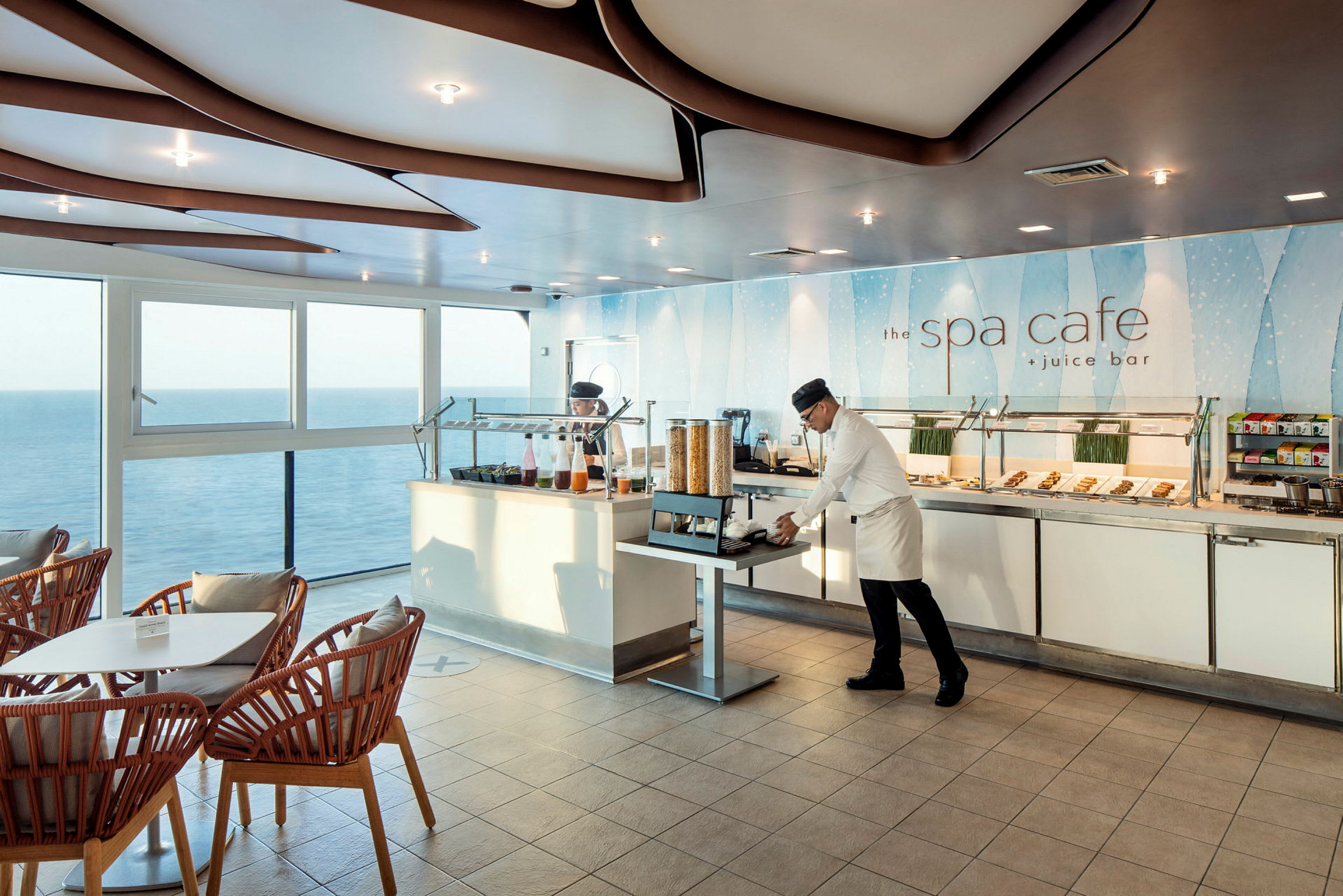 Et café med store vinduer, der giver udsigt over havet, med siddepladser og en buffet fyldt med mad og drikke. (AI-genereret tekst)