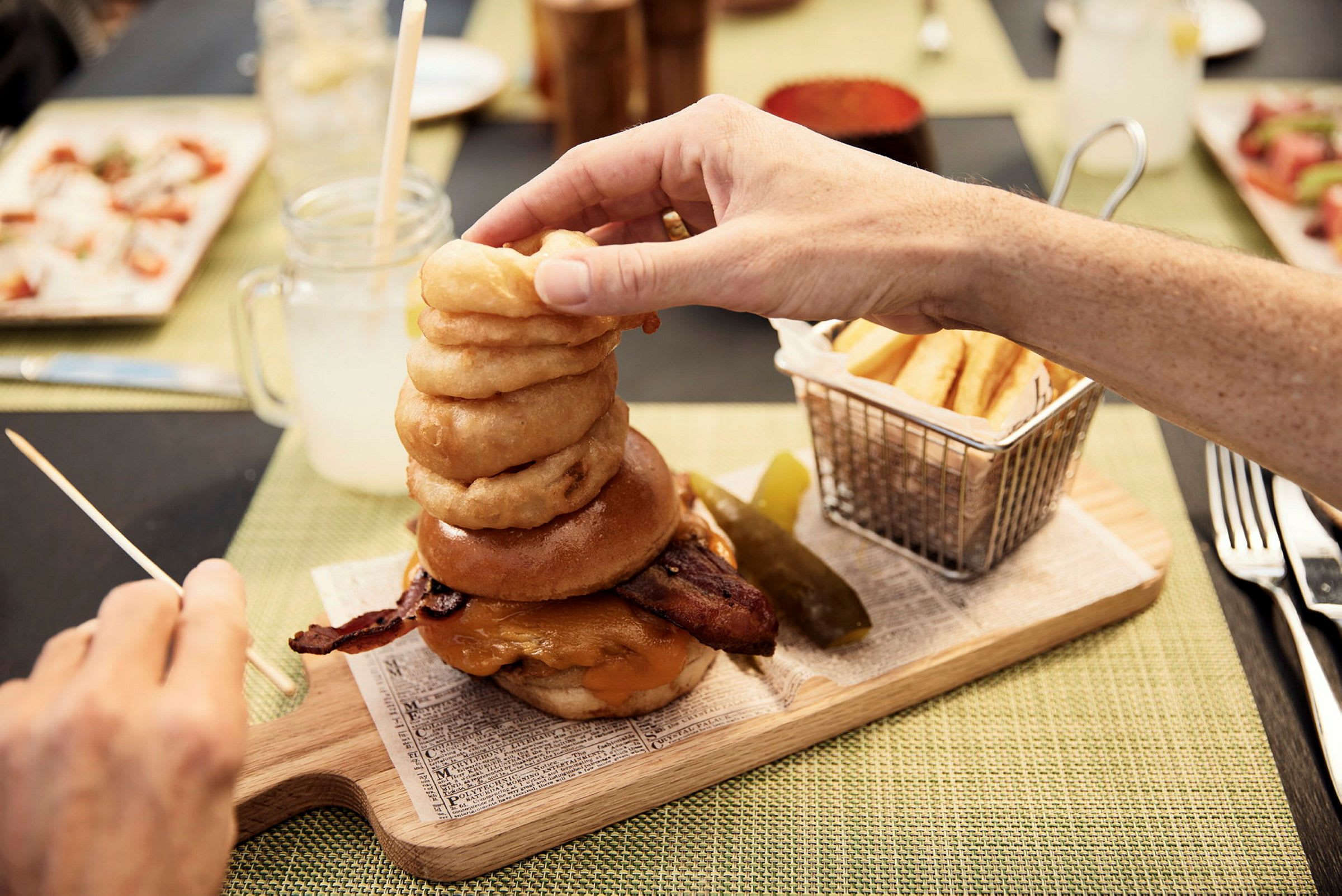 En burger med bacon, ost og løgringe, serveret med pommes frites og en agurkskive. (AI-genereret tekst)