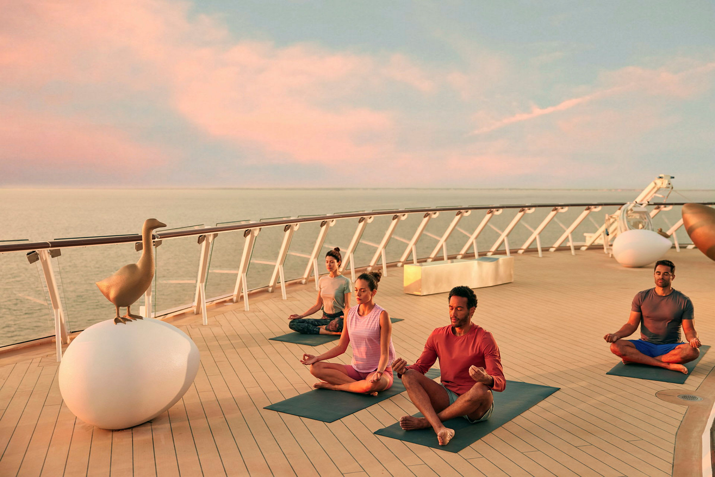 Personer praktiserer yoga på et krydstogtskibsdæk, ved havet under solnedgang. (AI-genereret tekst)