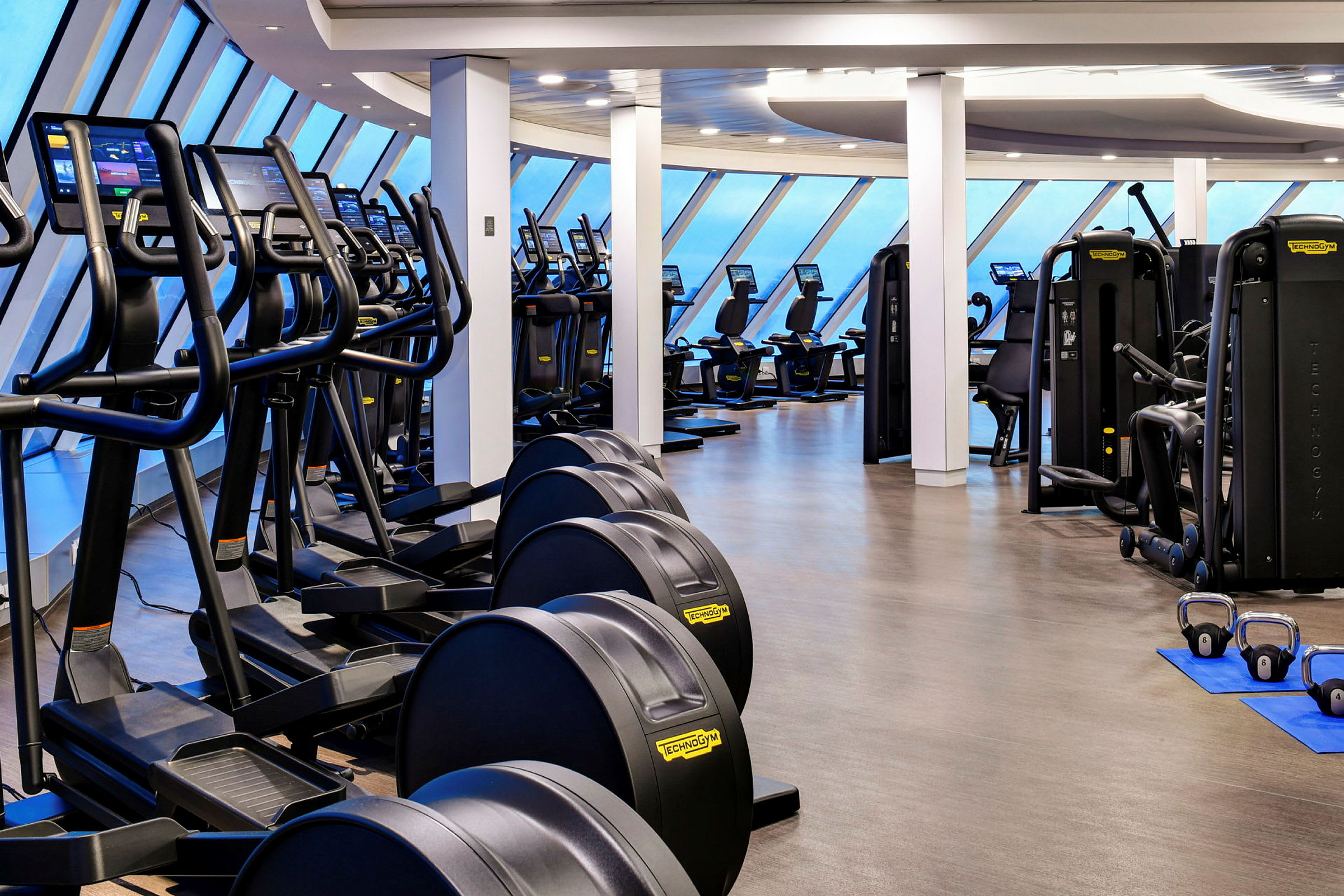 Billede af et fitnesscenter udstyret med forskellige træningsmaskiner og vinduer mod en blå himmel. (AI-genereret tekst)
