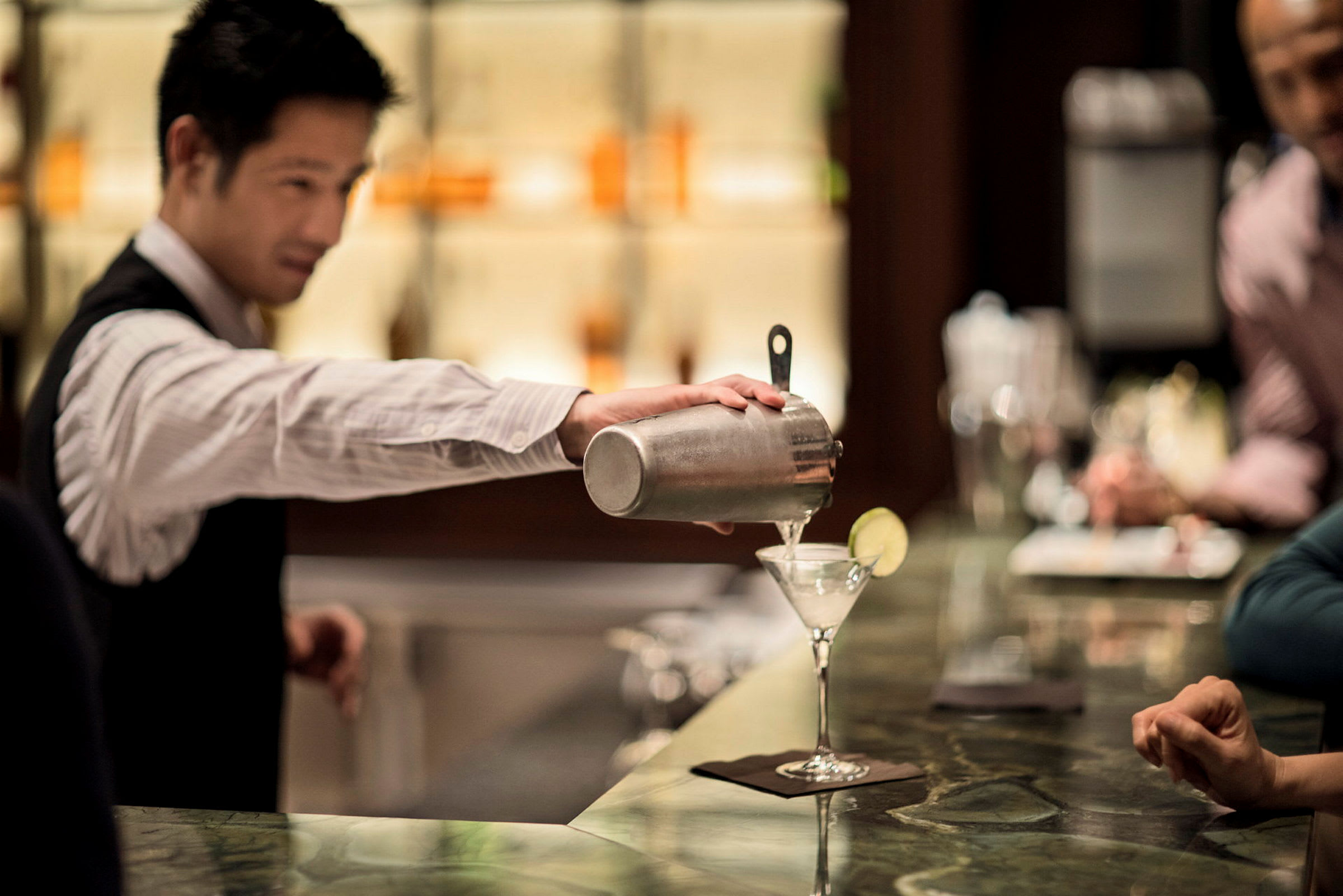 En serveringsperson, der hælder en drink op i et cocktailglas. (AI-genereret tekst)