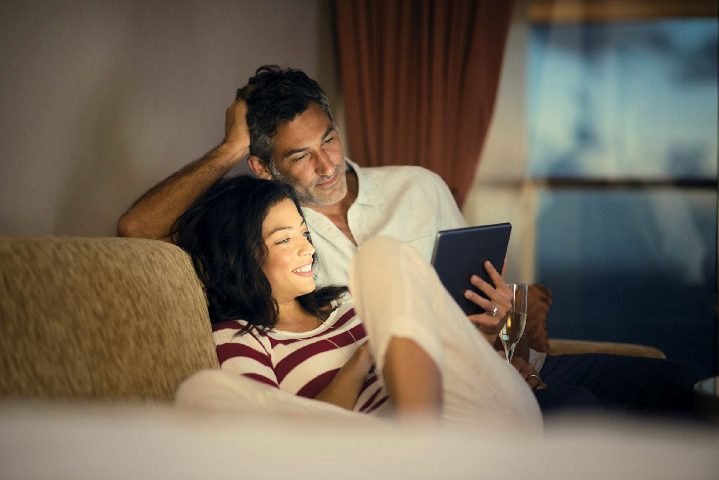 Person holder en tablet og et glas på en sofa. (AI-genereret tekst)