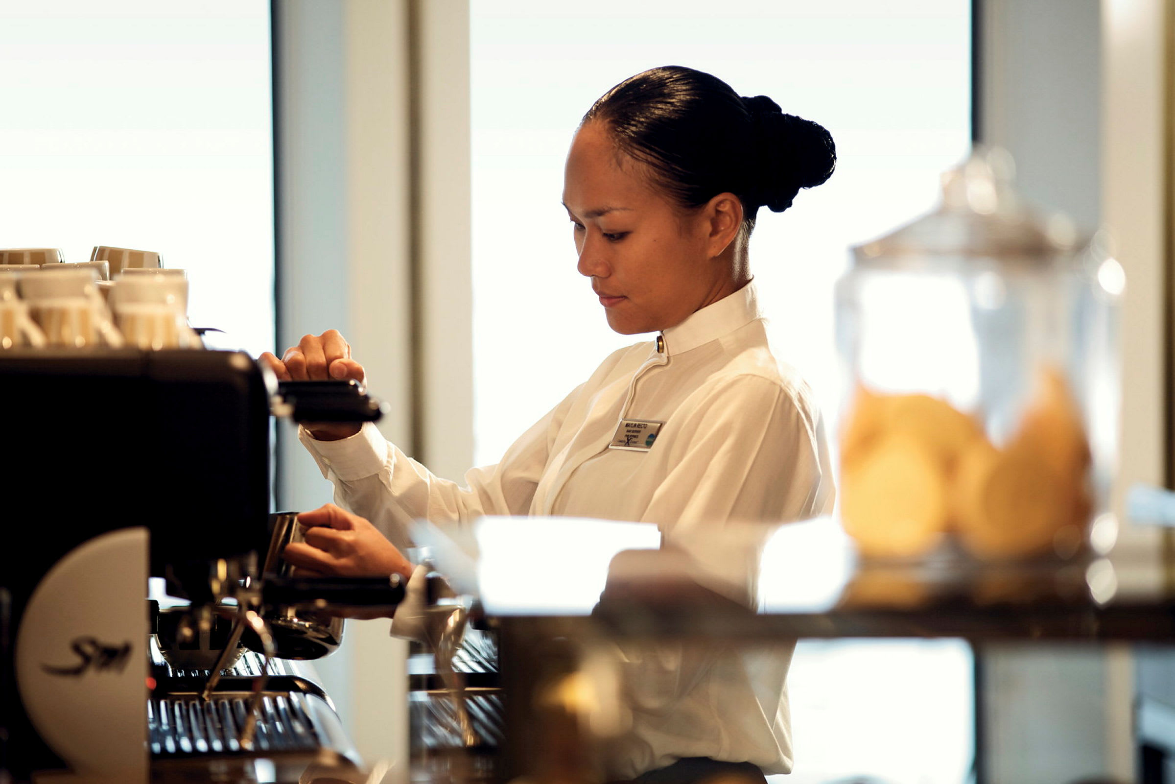 En person i uniform står ved en kaffemaskine og forbereder en drik. (AI-genereret tekst)