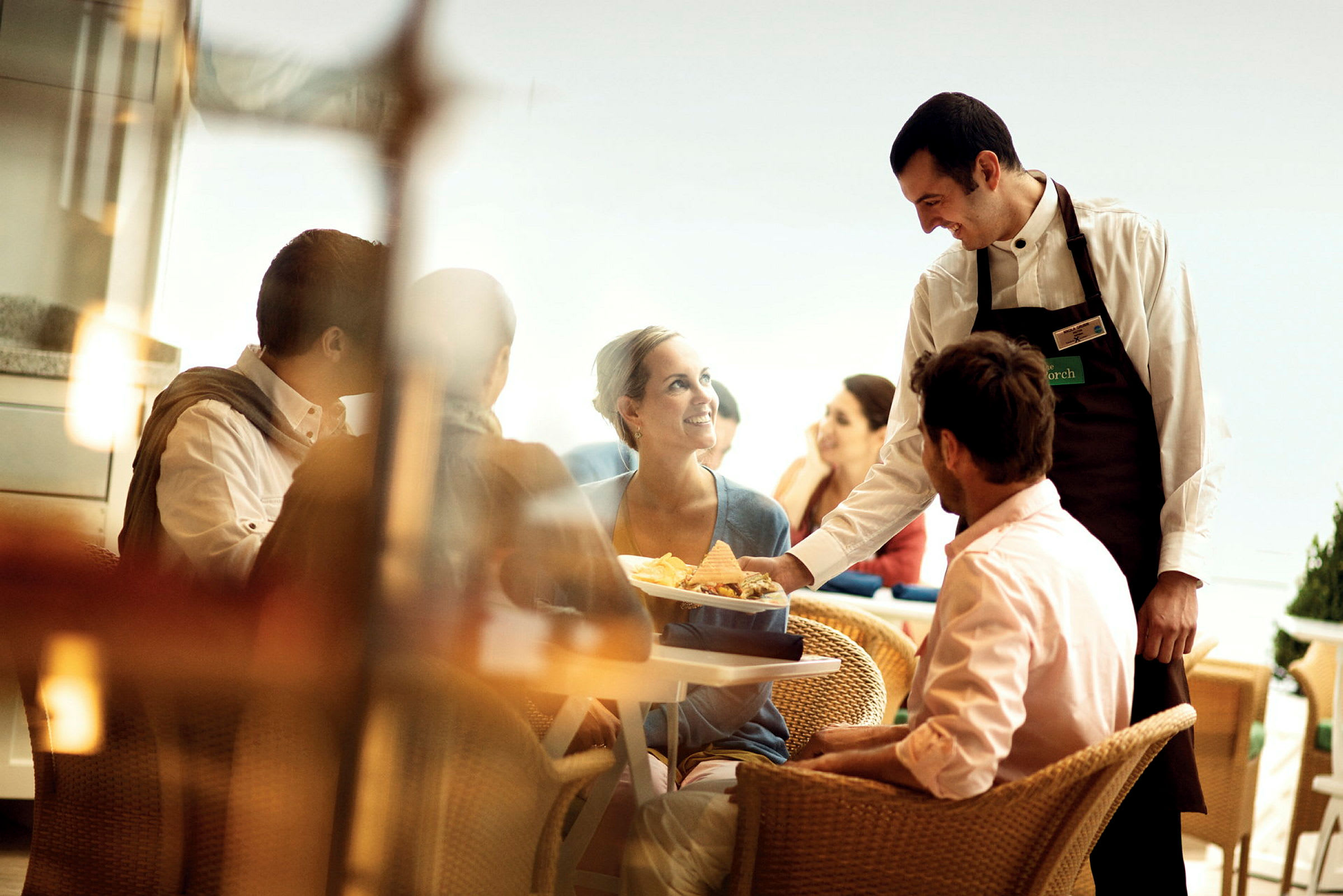 En tjener serverer mad til gæster ved et bord på en restaurant. (AI-genereret tekst)