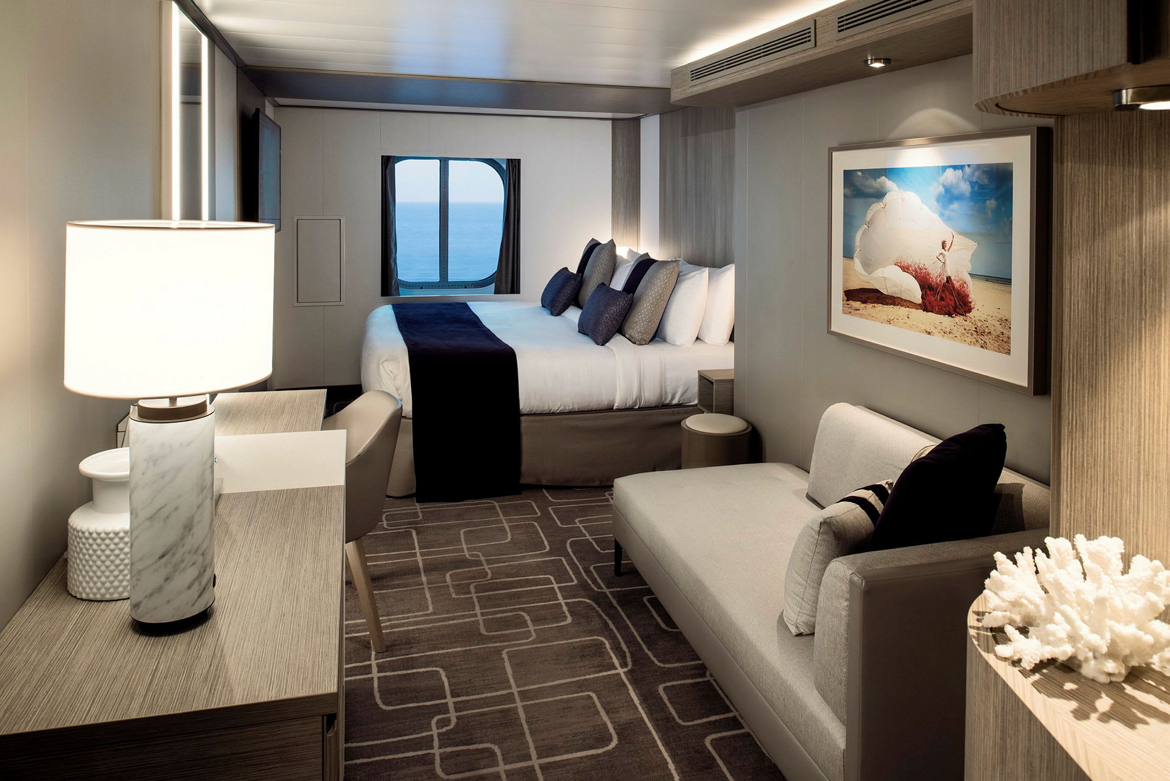 Moderne og elegant hotelværelse med en dobbeltseng, siddeområde og havudsigt gennem et rundt vindue. (AI-genereret tekst)