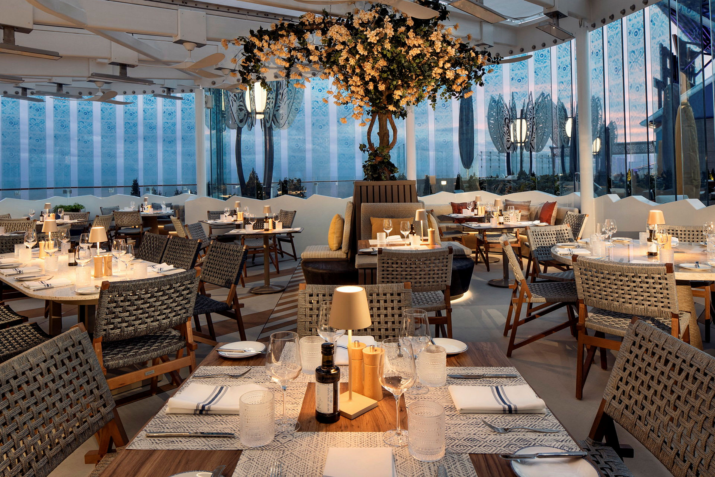 Restaurantmiljø med oprettede borde, stole og dekorativ belysning. I baggrunden ses en planteinstallation. (AI-genereret tekst)