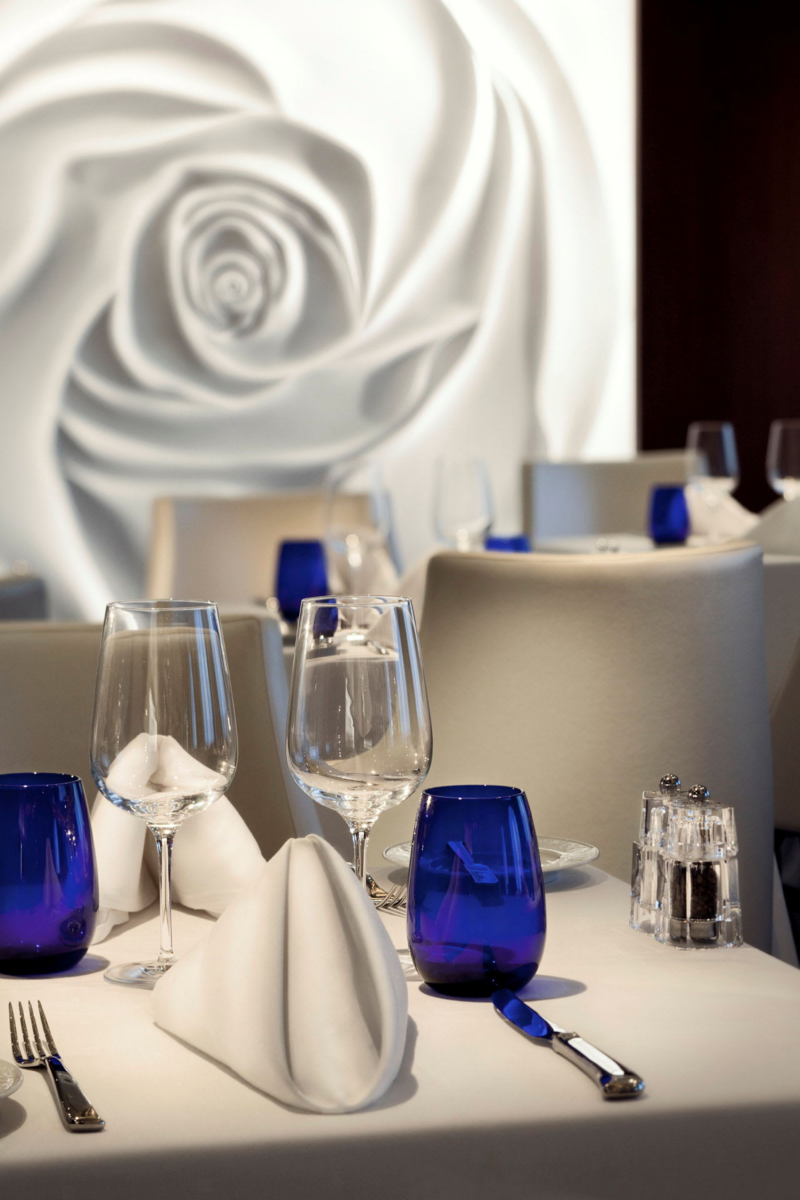 Billede af et dækket bord i en elegant restaurant med blå glas og hvide servietter. (AI-genereret tekst)