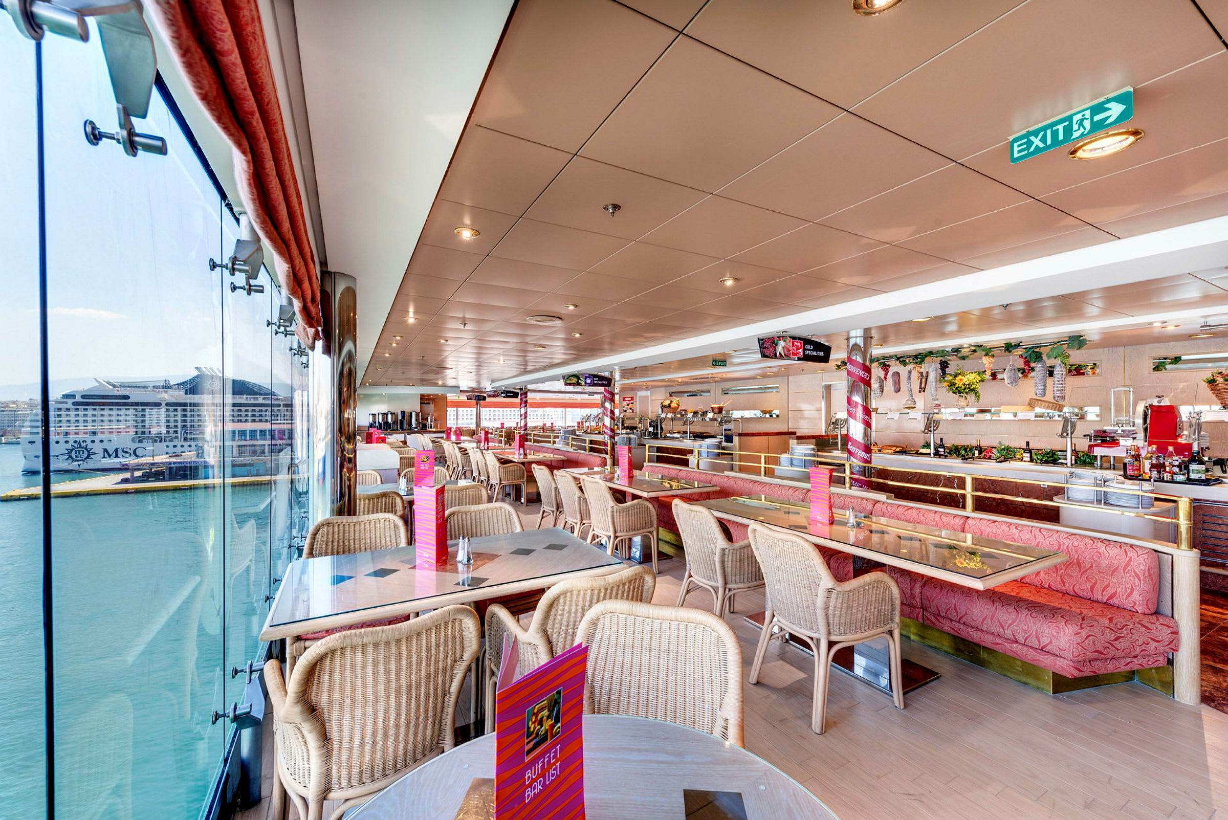 Indendørs billede af en lys restaurant med siddepladser og store vinduer med udsigt til et skib ved en havn. (AI-genereret tekst)