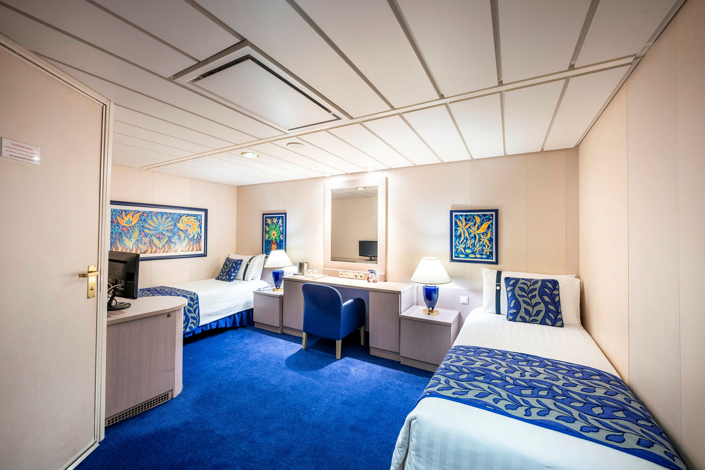 Hotelværelse med to enkeltsenge, blå indretning og bord mellem sengene. Vægdekoration i farver er til stede. (AI-genereret tekst)