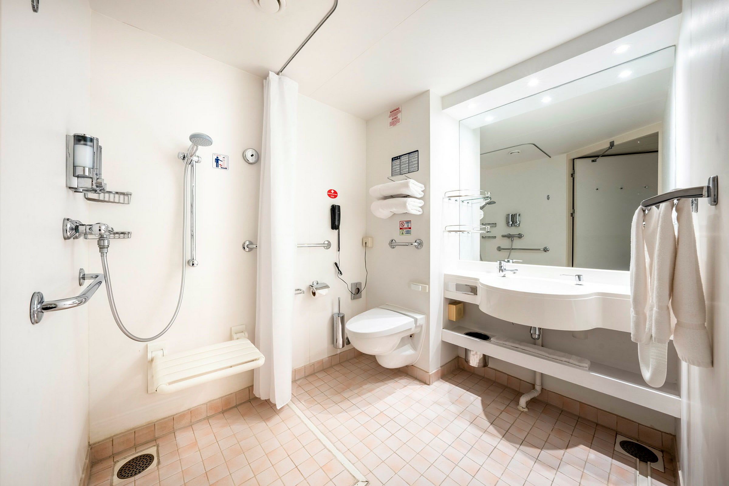 Badeværelse med handicapvenlig bruser, toilet og håndvask. (AI-genereret tekst)