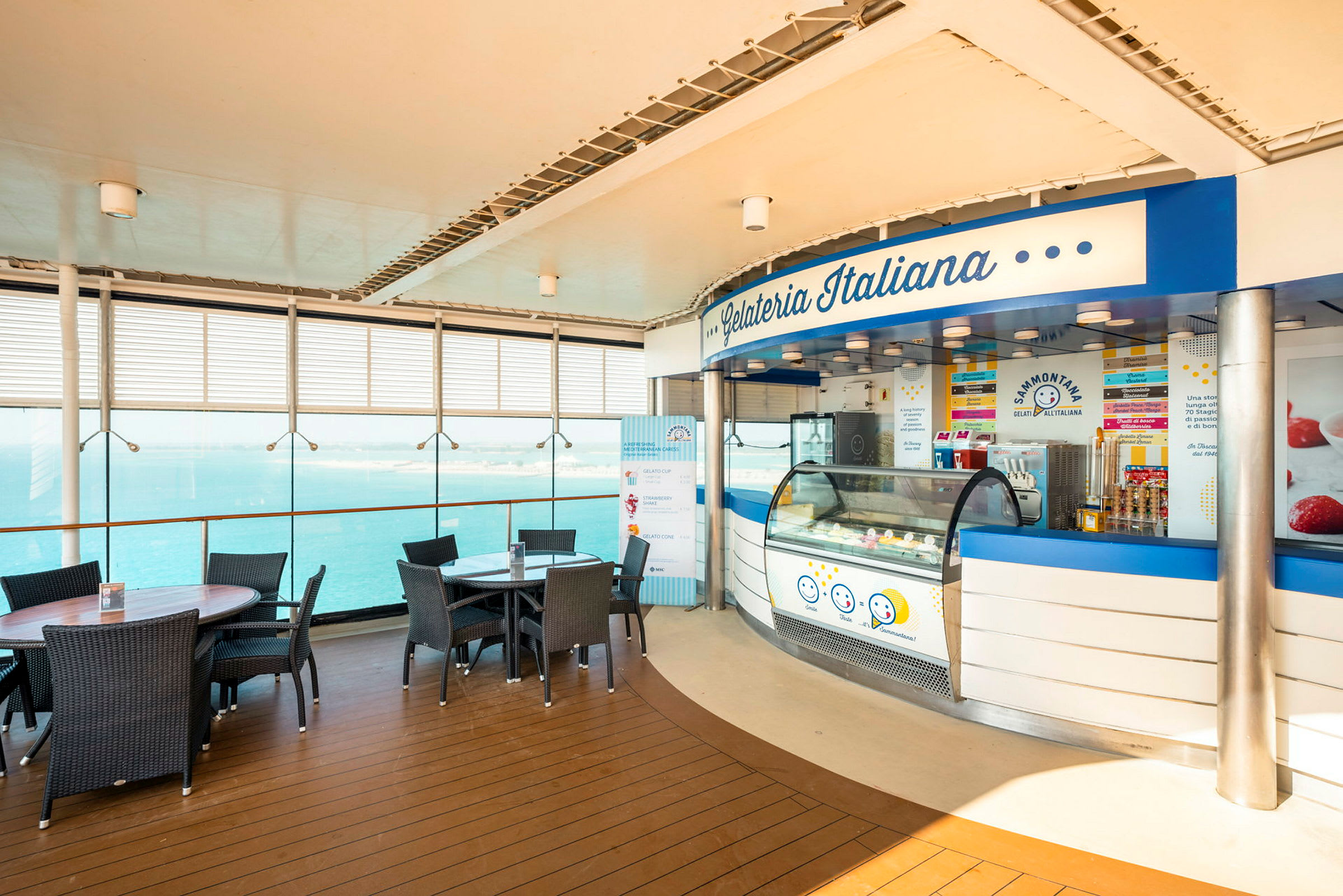 En isbod med navnet Gelateria Italiana beliggende ved et område med borde og stole nær glasvinduer med udsigt over havet. (AI-genereret tekst)