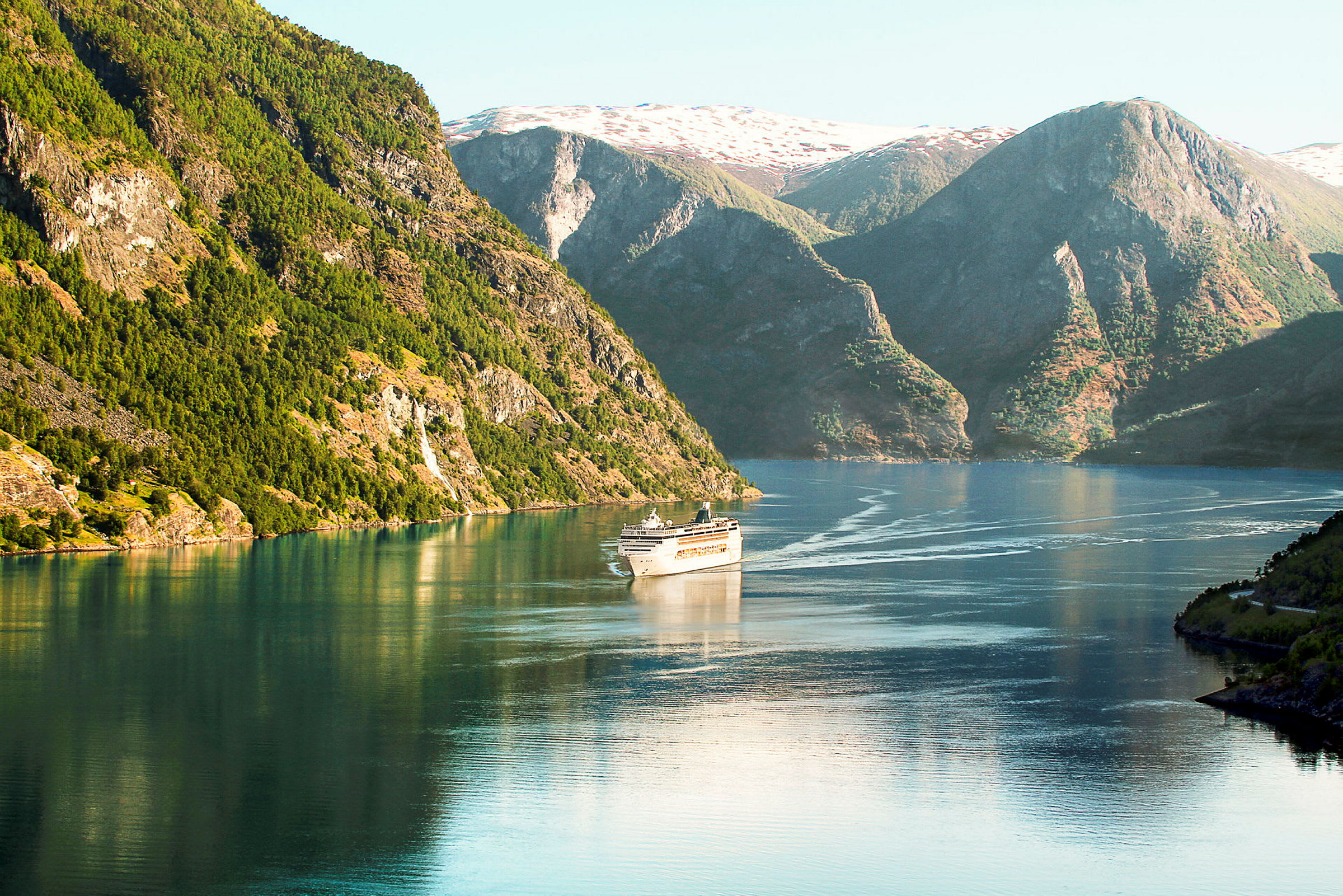Billede af et krydstogtskib, der sejler gennem en fjord med høje bjergsider og klart vand. (AI-genereret tekst)