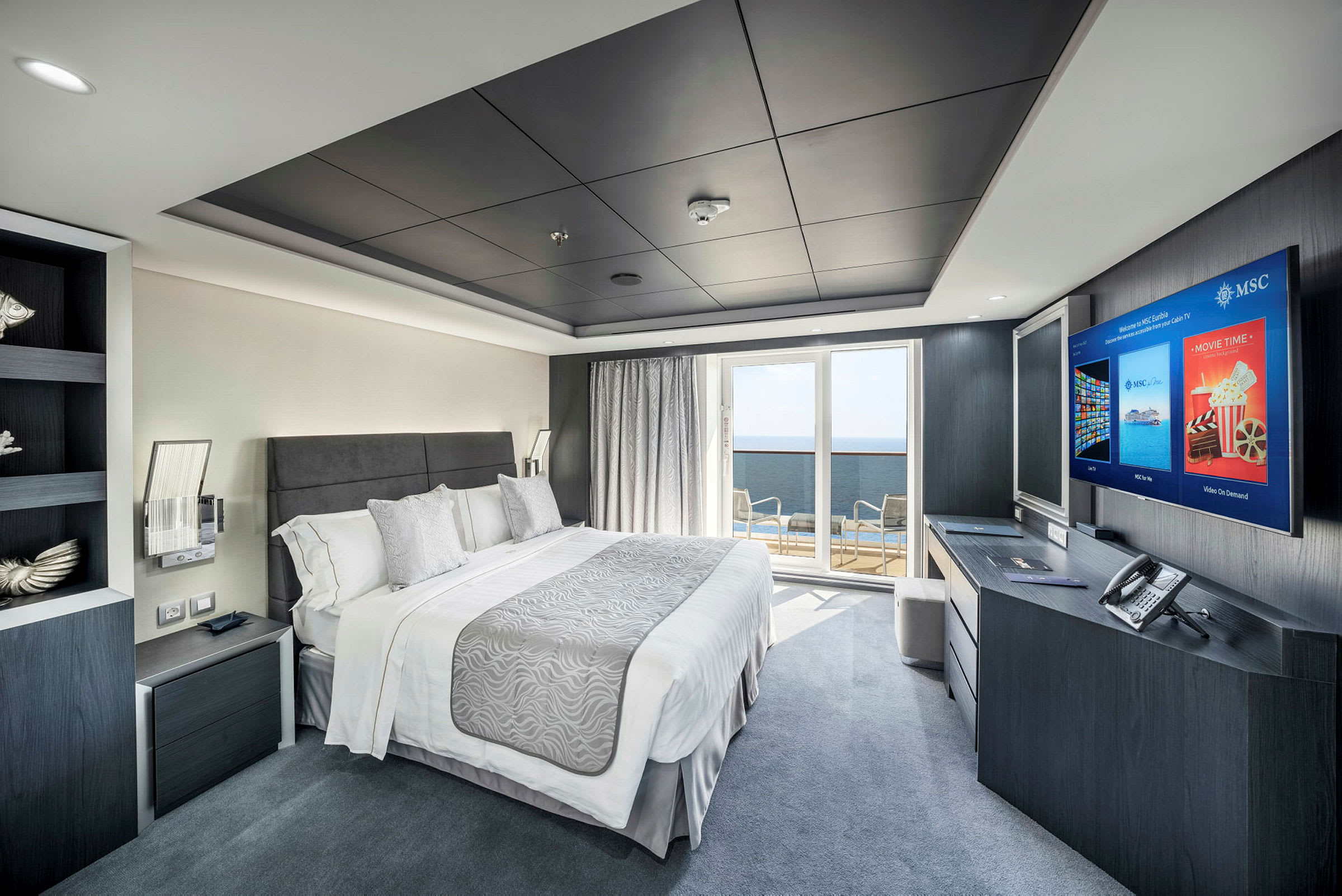 Et moderne hotelværelse med en dobbeltseng, skrivebord med TV, balkon med udsigt og elegant indretning. (AI-genereret tekst)