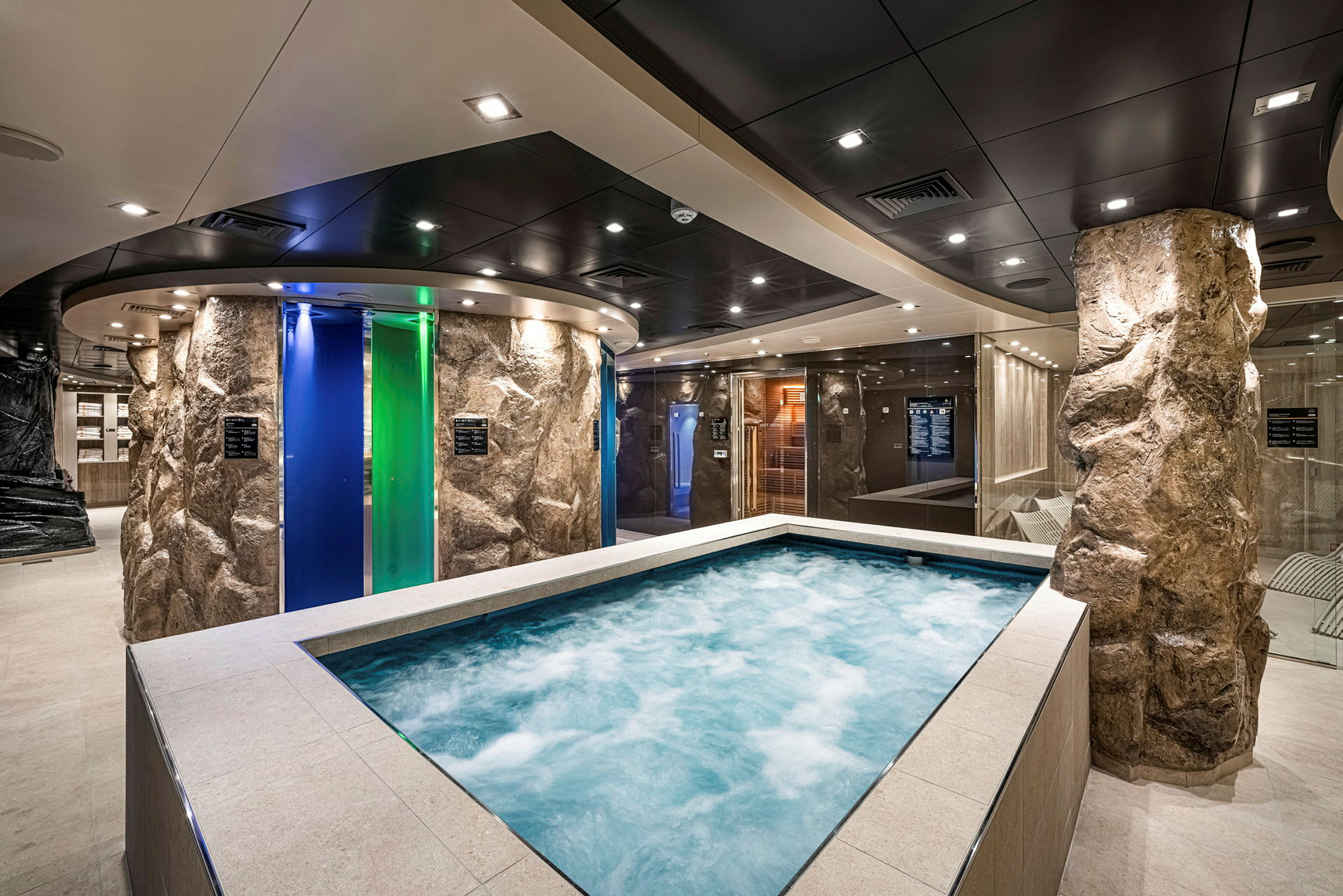 Et spaområde med en jacuzzi omgivet af stenlignende søjler og farvede glasdøre. (AI-genereret tekst)