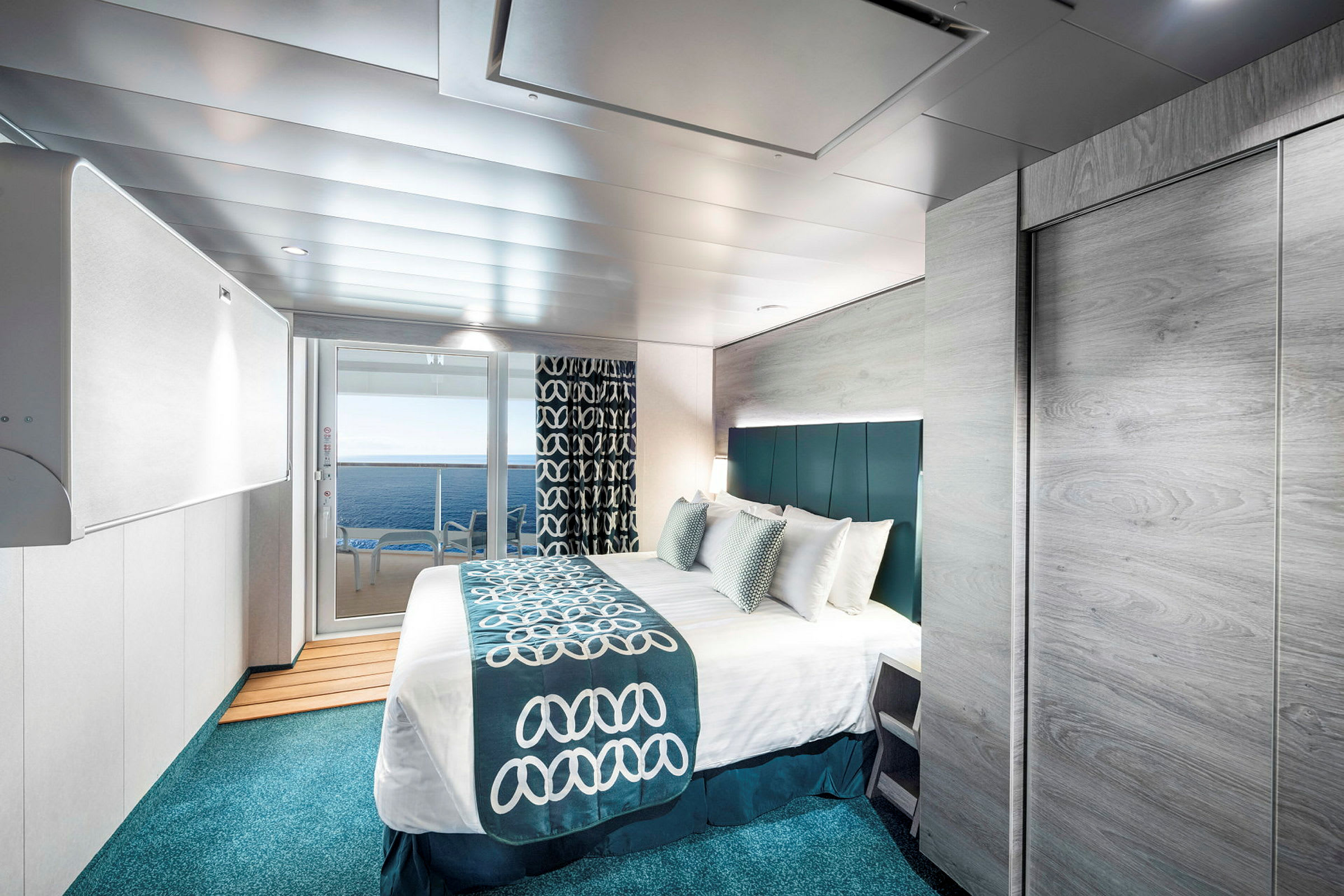 Et moderne indrettet hotelværelse med en stor seng, udsigt over havet gennem glasdøre og smagfulde blå og hvide detaljer i indretningen. (AI-genereret tekst)