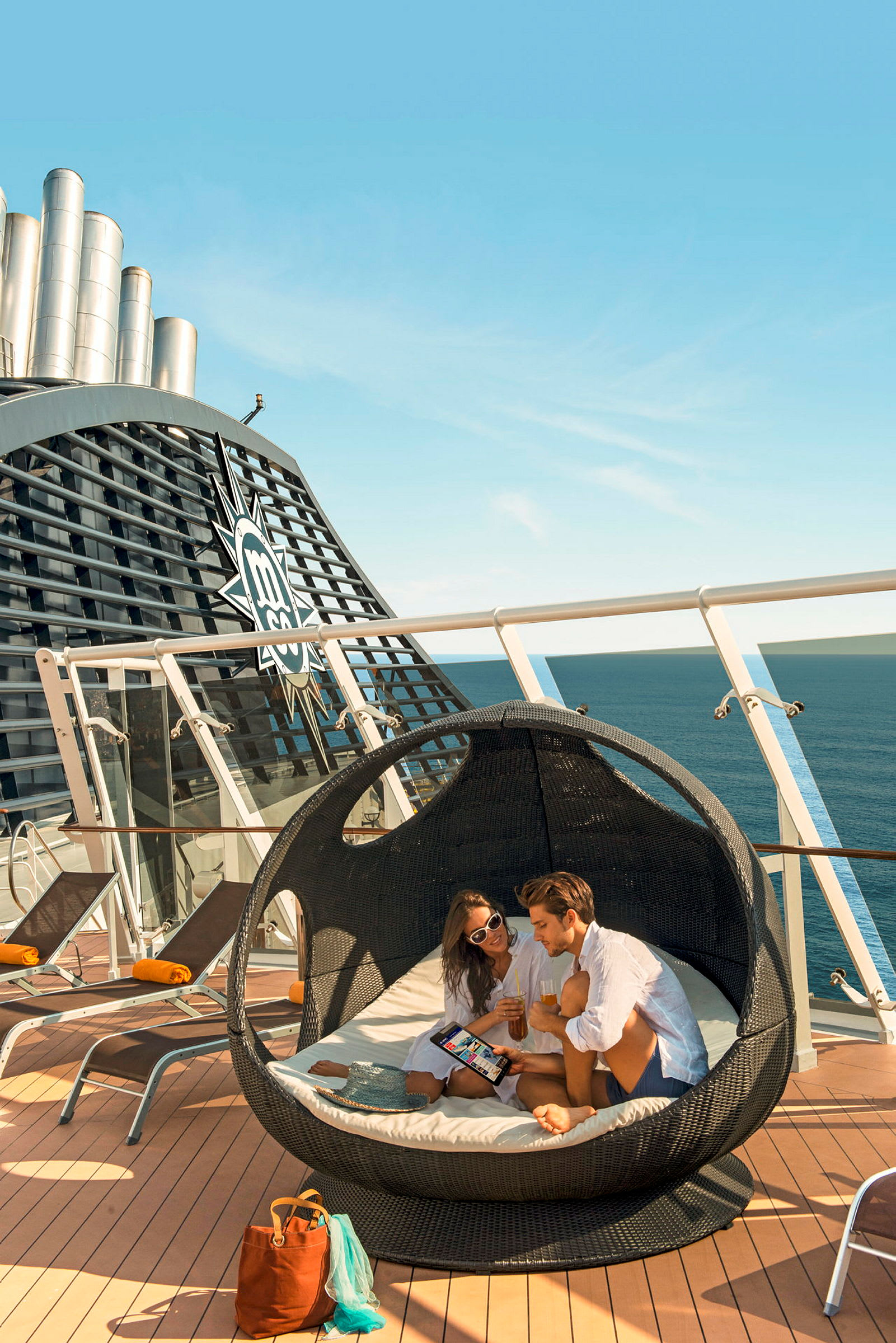 Personer sidder i en rund loungestol med havet i baggrunden på et krydstogtskib. (AI-genereret tekst)