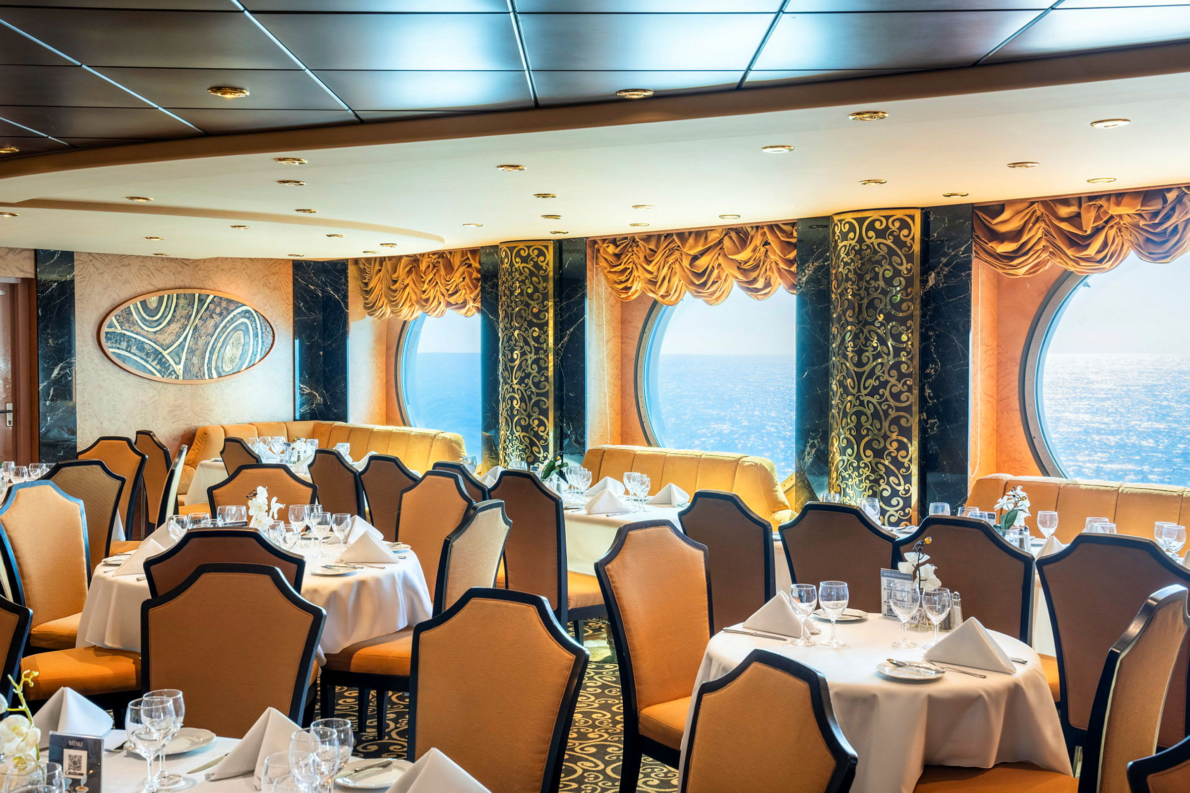 En elegant restaurant med dækkede borde, beige stole og store vinduer med havudsigt. (AI-genereret tekst)