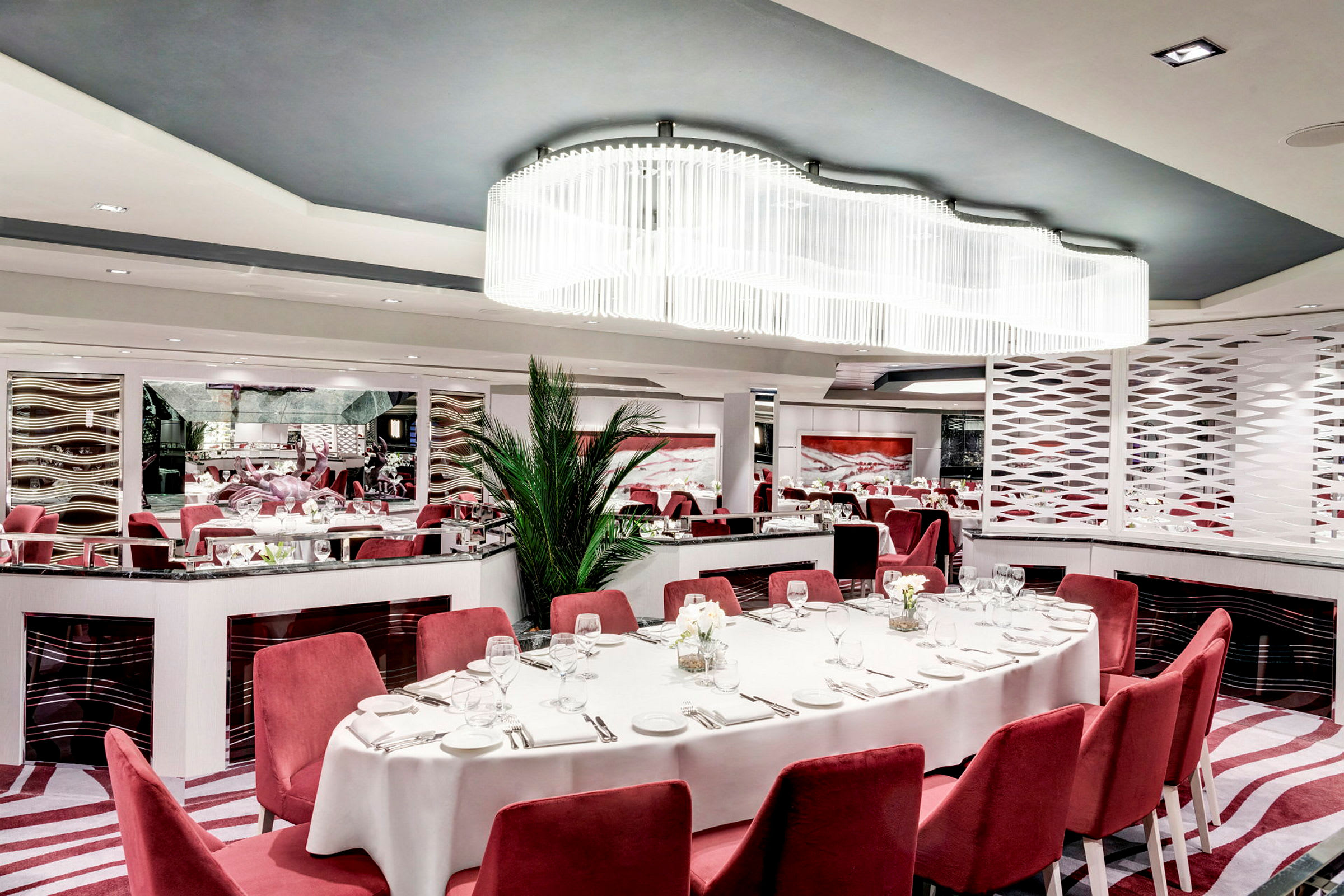 Elegant restaurant med røde stole, hvid dug og moderne interiør. (AI-genereret tekst)