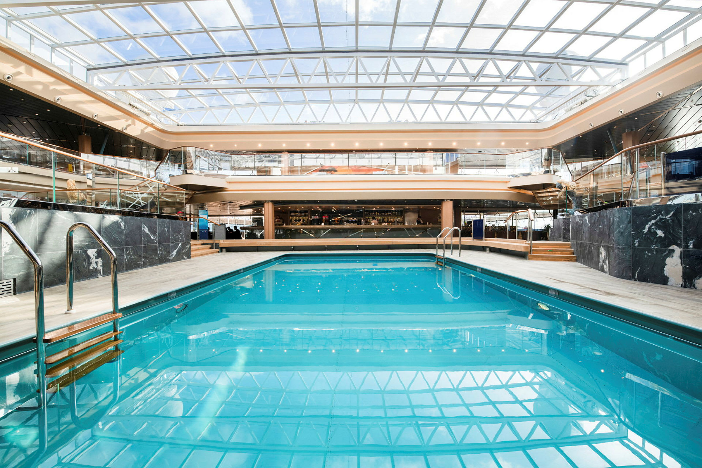 Indendørs pool med glastag og omkringliggende trapper og balkoner. (AI-genereret tekst)