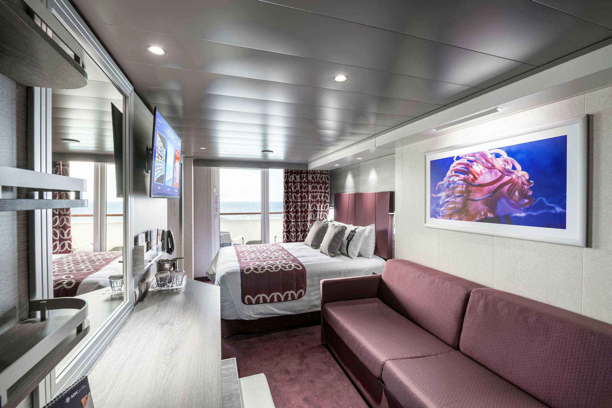 Interiørbillede af et hotelværelse med en seng, en sofa og havudsigt fra en balkon. (AI-genereret tekst)