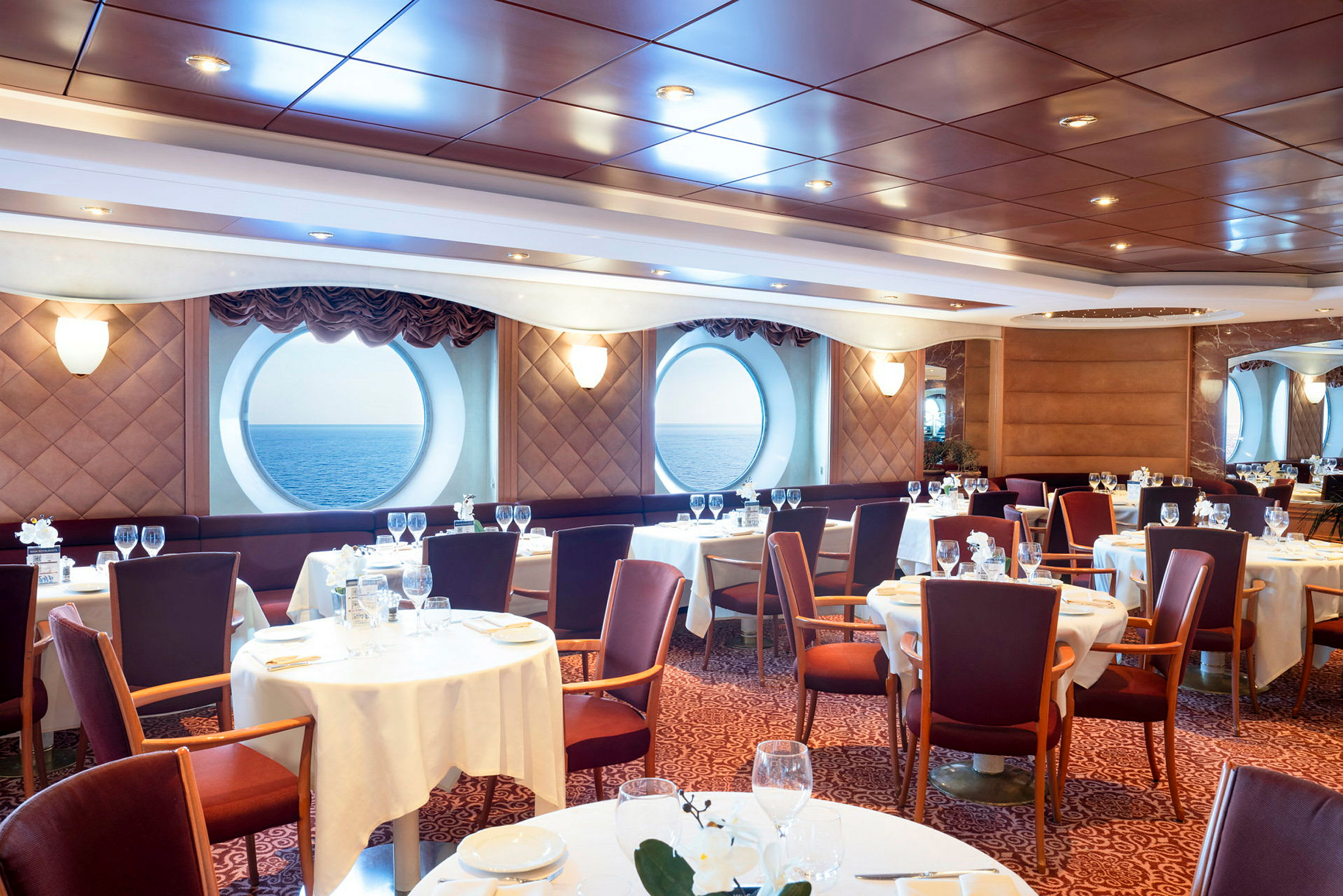 En elegant spisestue med runde vinduer med udsigt til havet. (AI-genereret tekst)