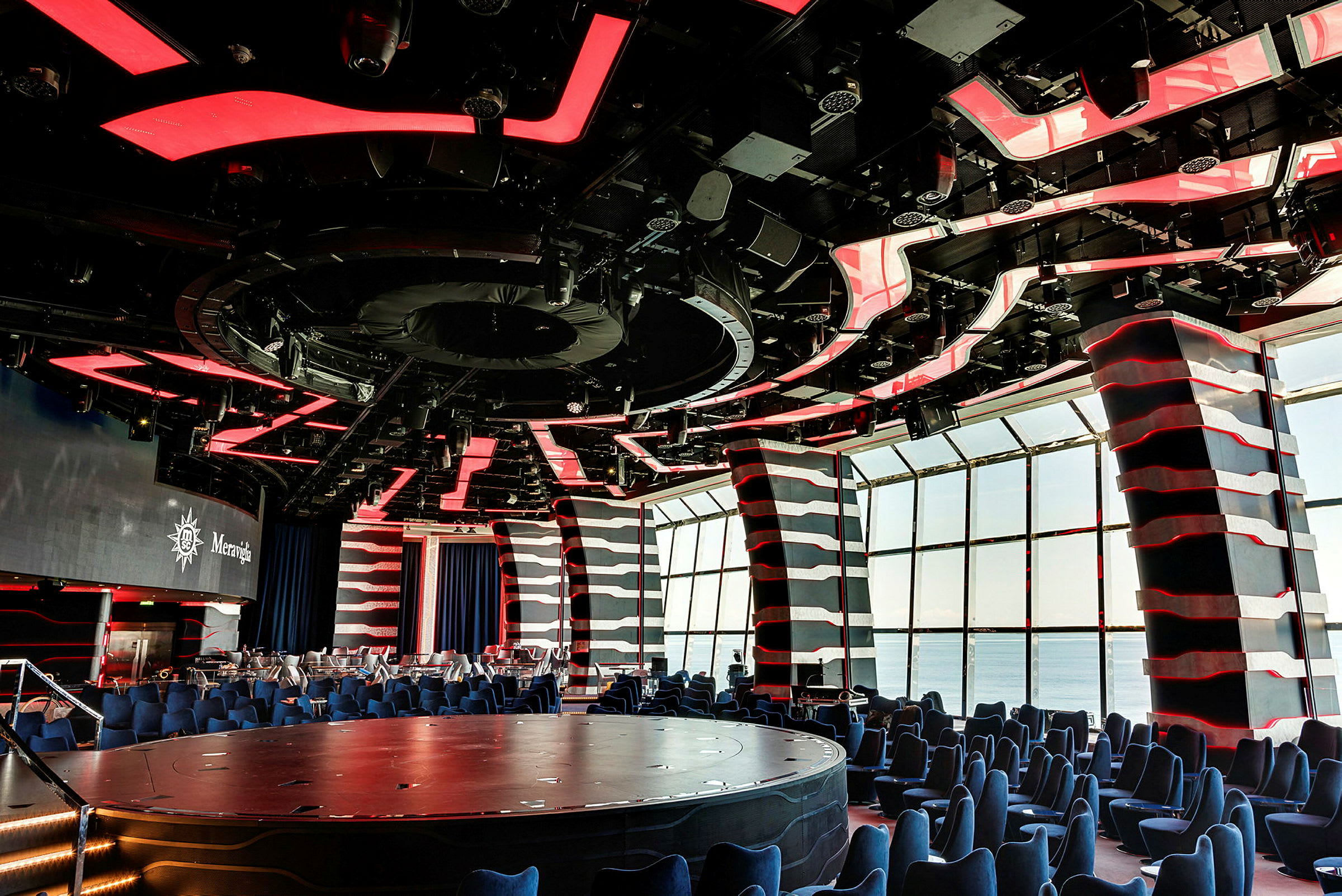 Et moderne auditorium med rødt og sort loft, siddepladser og store vinduer. (AI-genereret tekst)