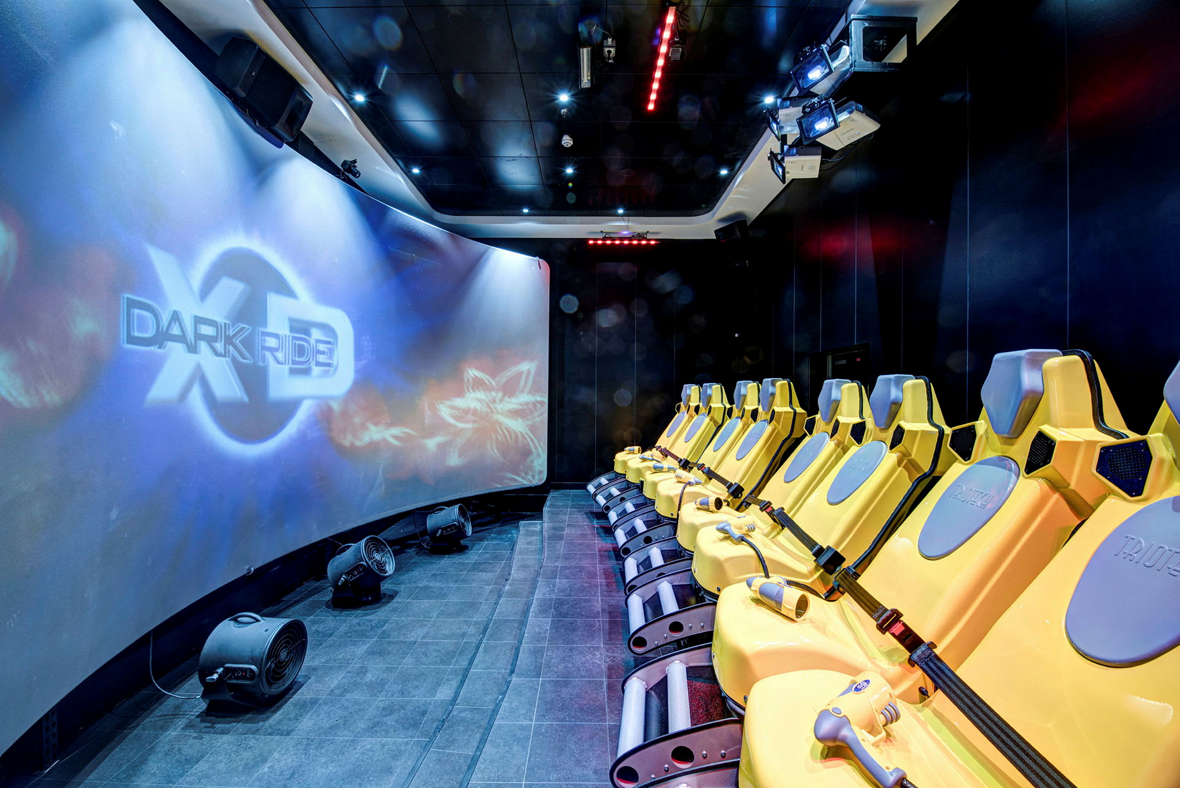 Række af gule sæder foran en stor buet skærm med teksten "XD Dark Ride". (AI-genereret tekst)