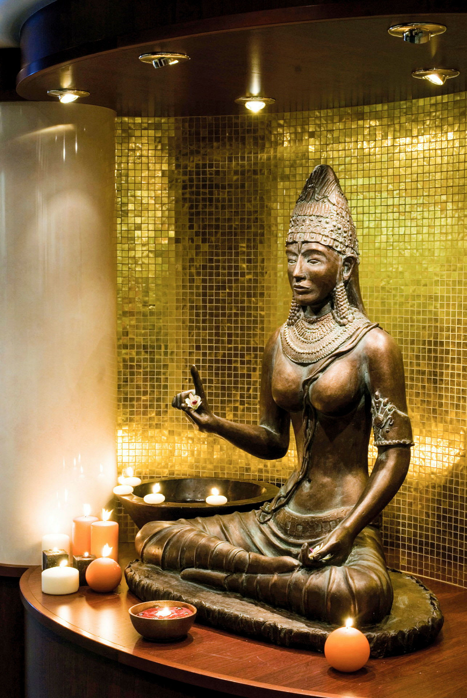 Statue af en buddhistisk figur foran en gylden mosaikvæg omgivet af tændte lys. (AI-genereret tekst)