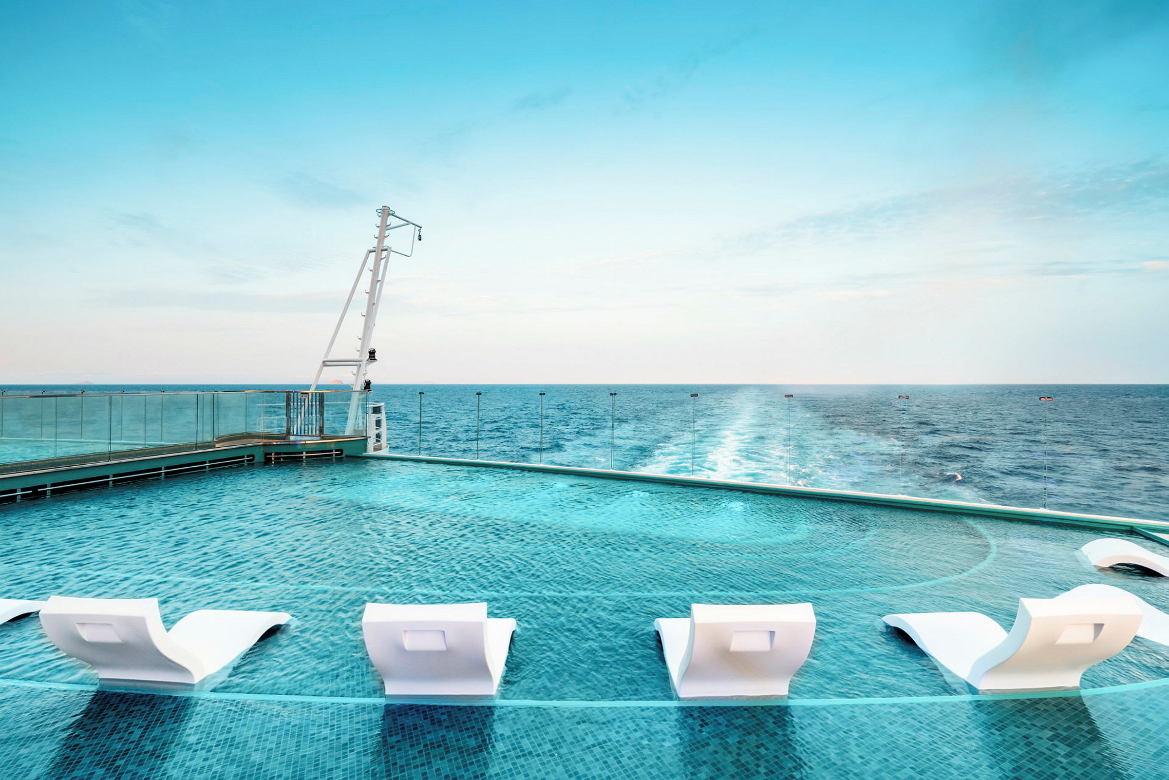 Pool med hvide liggestole ved havet. (AI-genereret tekst)
