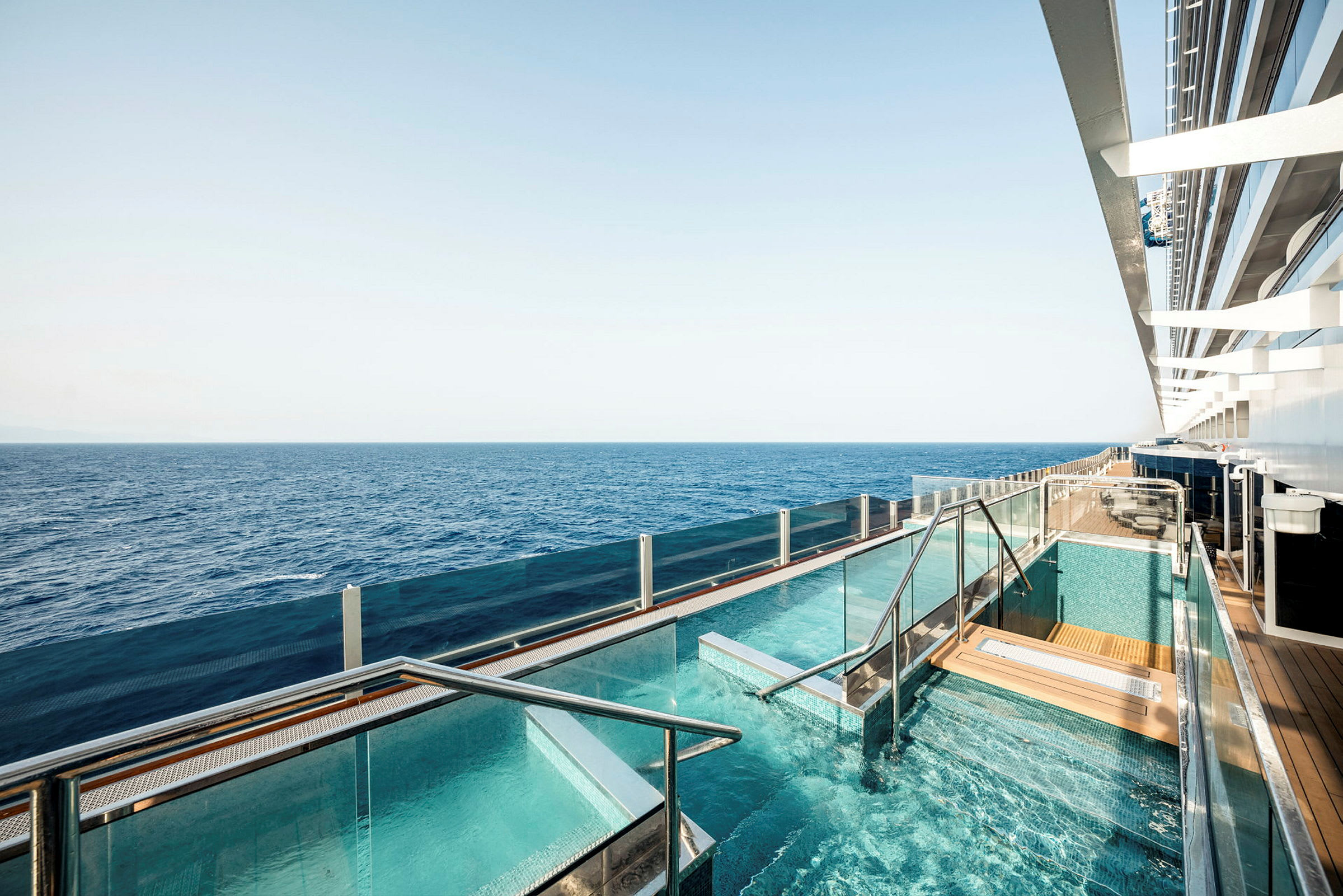 En pool med glasrækværk på et skib med havet i baggrunden. (AI-genereret tekst)