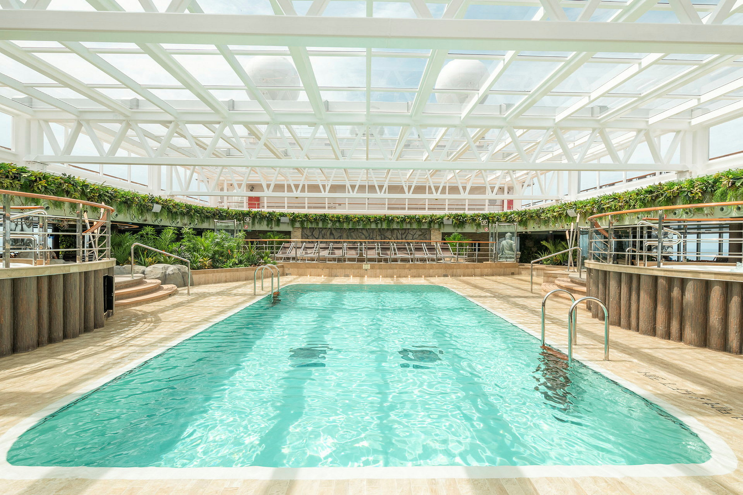 En indendørs pool med liggestole og grønne planter rundt omkring. (AI-genereret tekst)