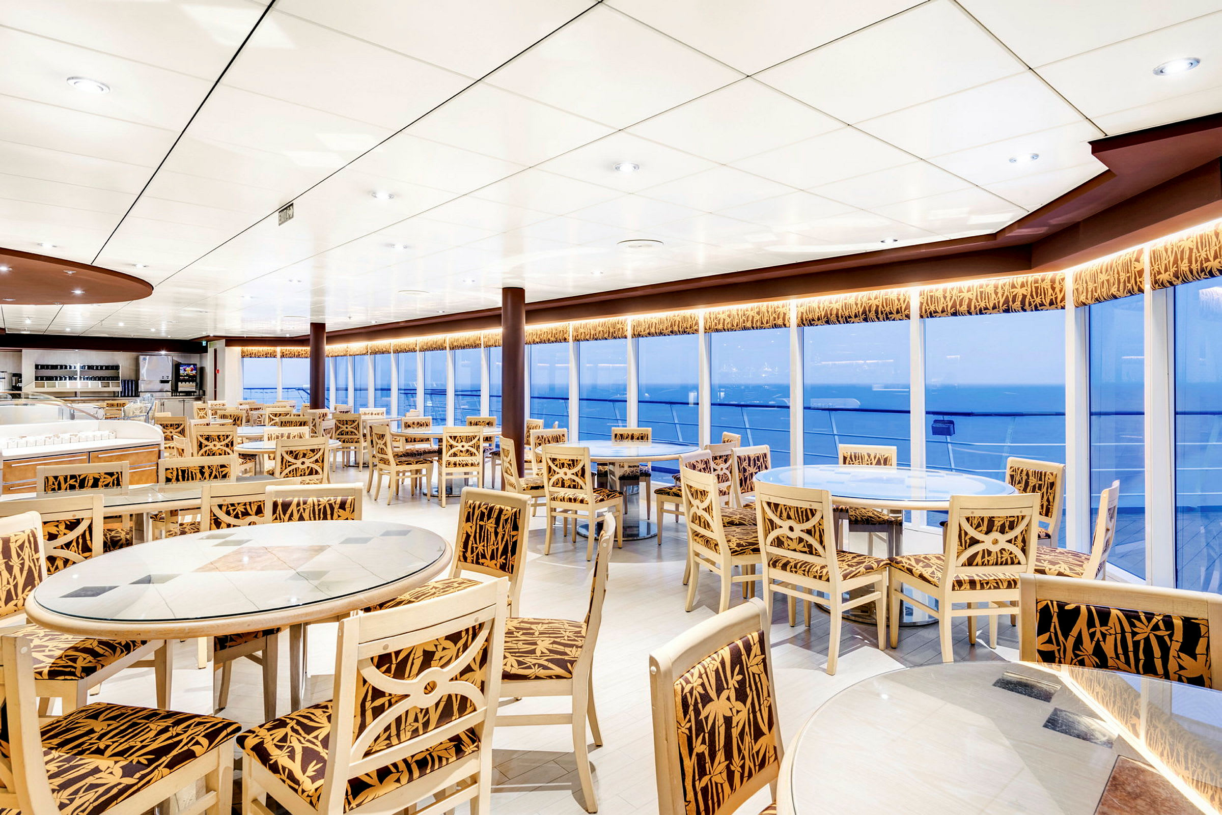 Et restaurantområde med borde og stole foran store vinduer. (AI-genereret tekst)