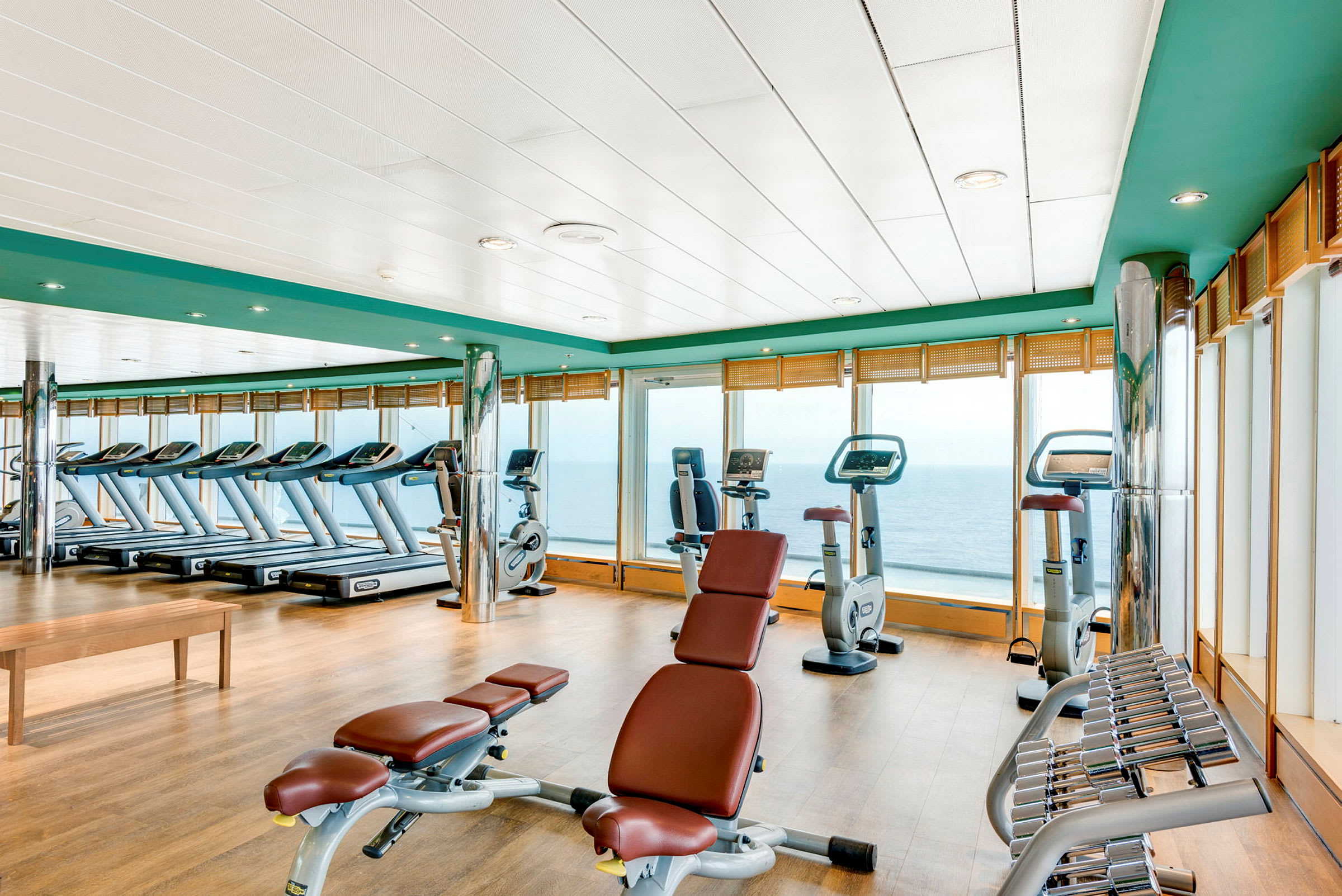 Et fitnesscenter med træningsmaskiner og frie vægte med udsigt over havet. (AI-genereret tekst)