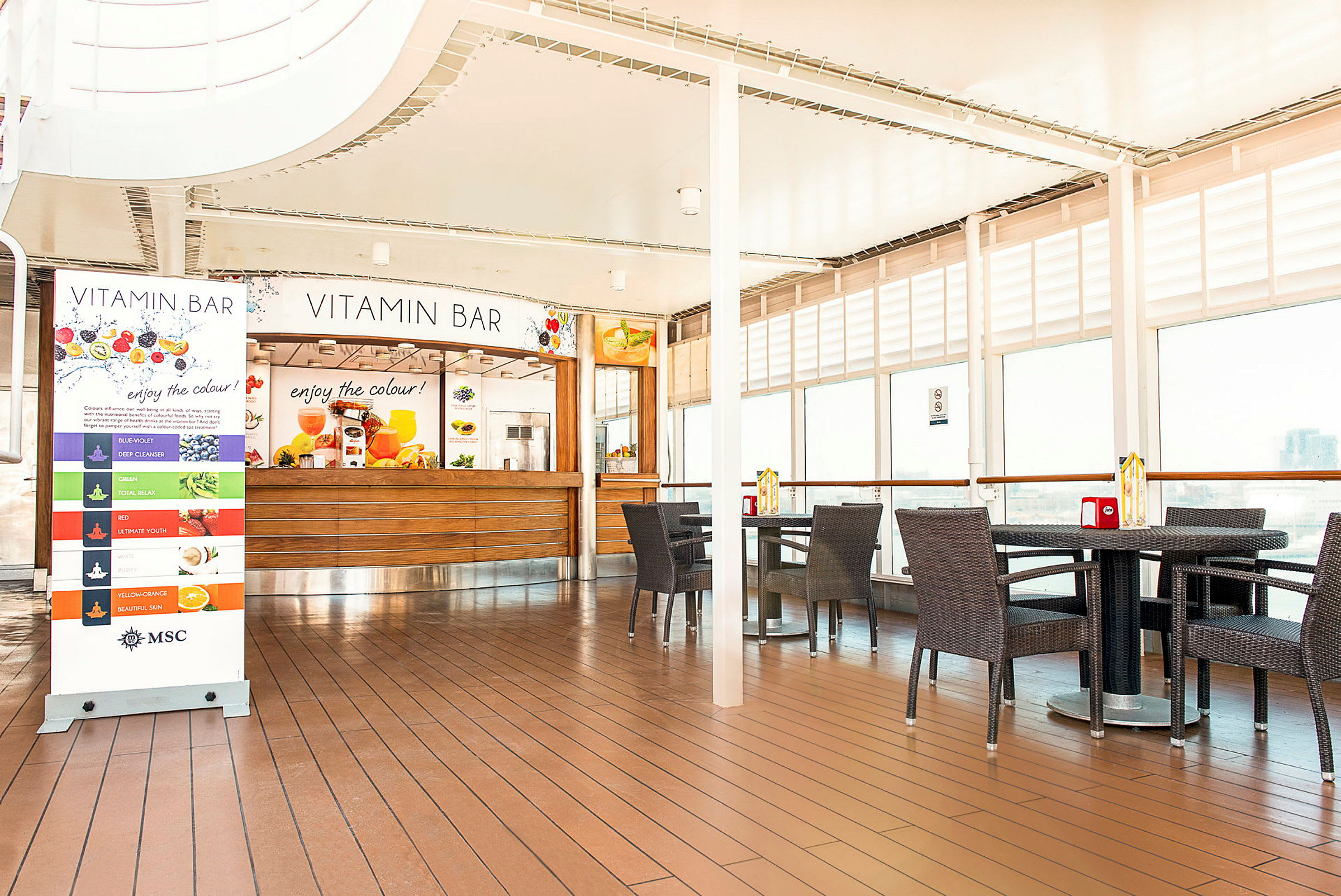 Indendørsmiljø med en juicebar med navnet Vitamin Bar, omgivet af borde og stole. (AI-genereret tekst)