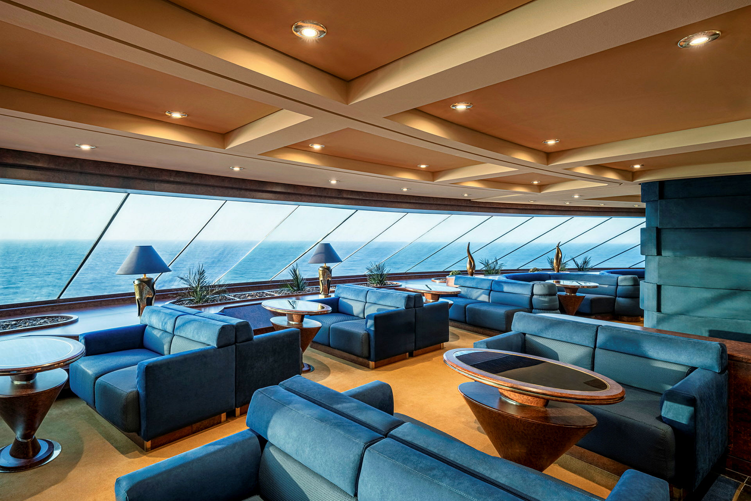 Lounge med sofaer og borde, store glasvinduer med udsigt over havet. (AI-genereret tekst)