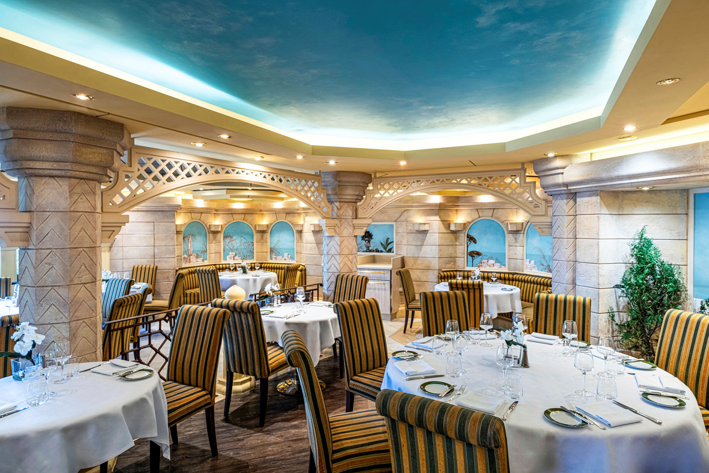 Interiør af en restaurant med buede lofter, dekorerede vægge, dækkede borde og stribede stole. (AI-genereret tekst)