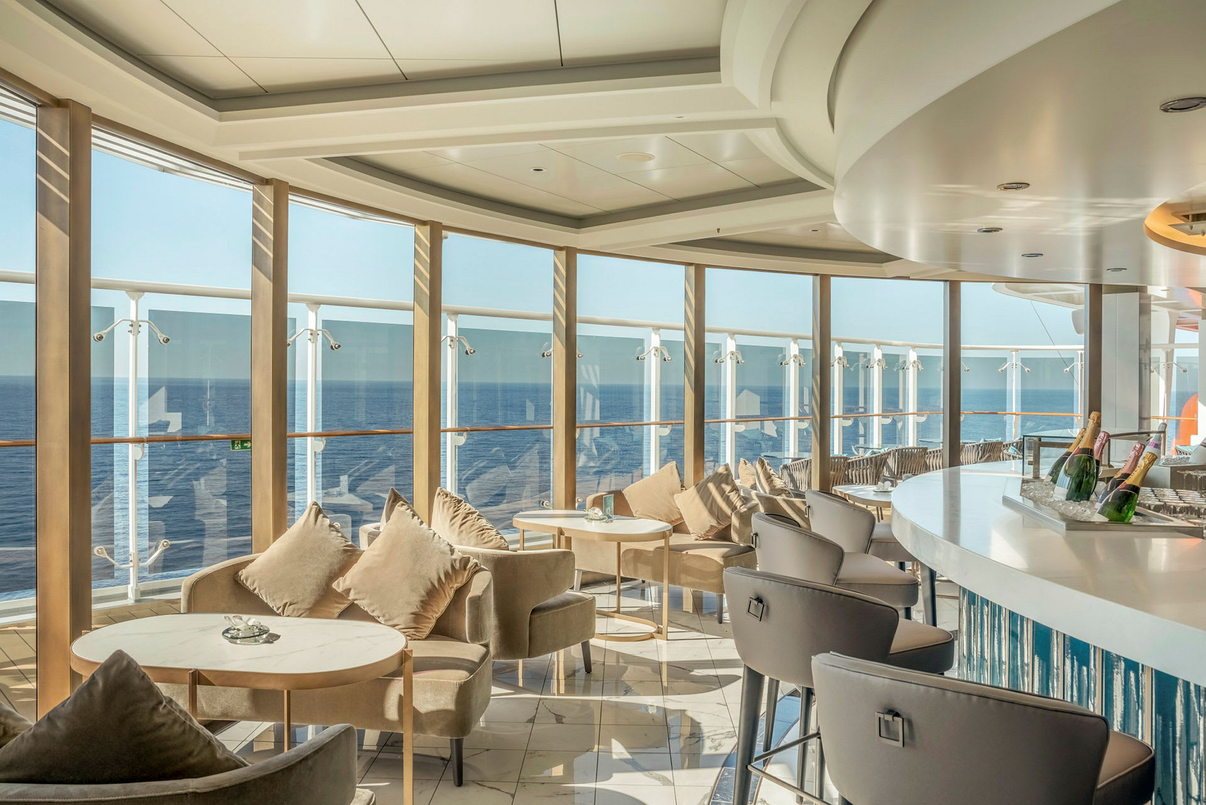 En elegant lounge med siddepladser og borde ved store vinduer med udsigt over havet. (AI-genereret tekst)