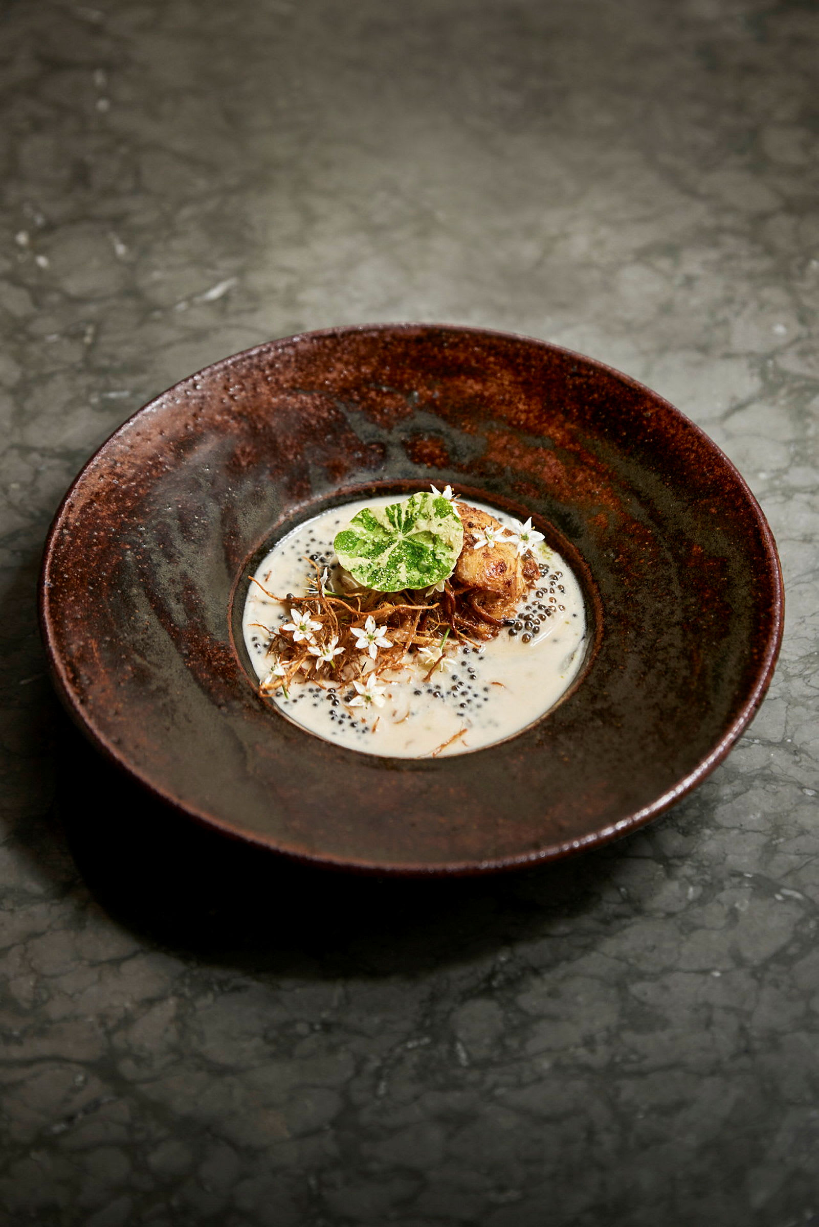 Nærbillede af en ret anrettet i en mørk skål, med cremet sauce og dekorative ingredienser. (AI-genereret tekst)