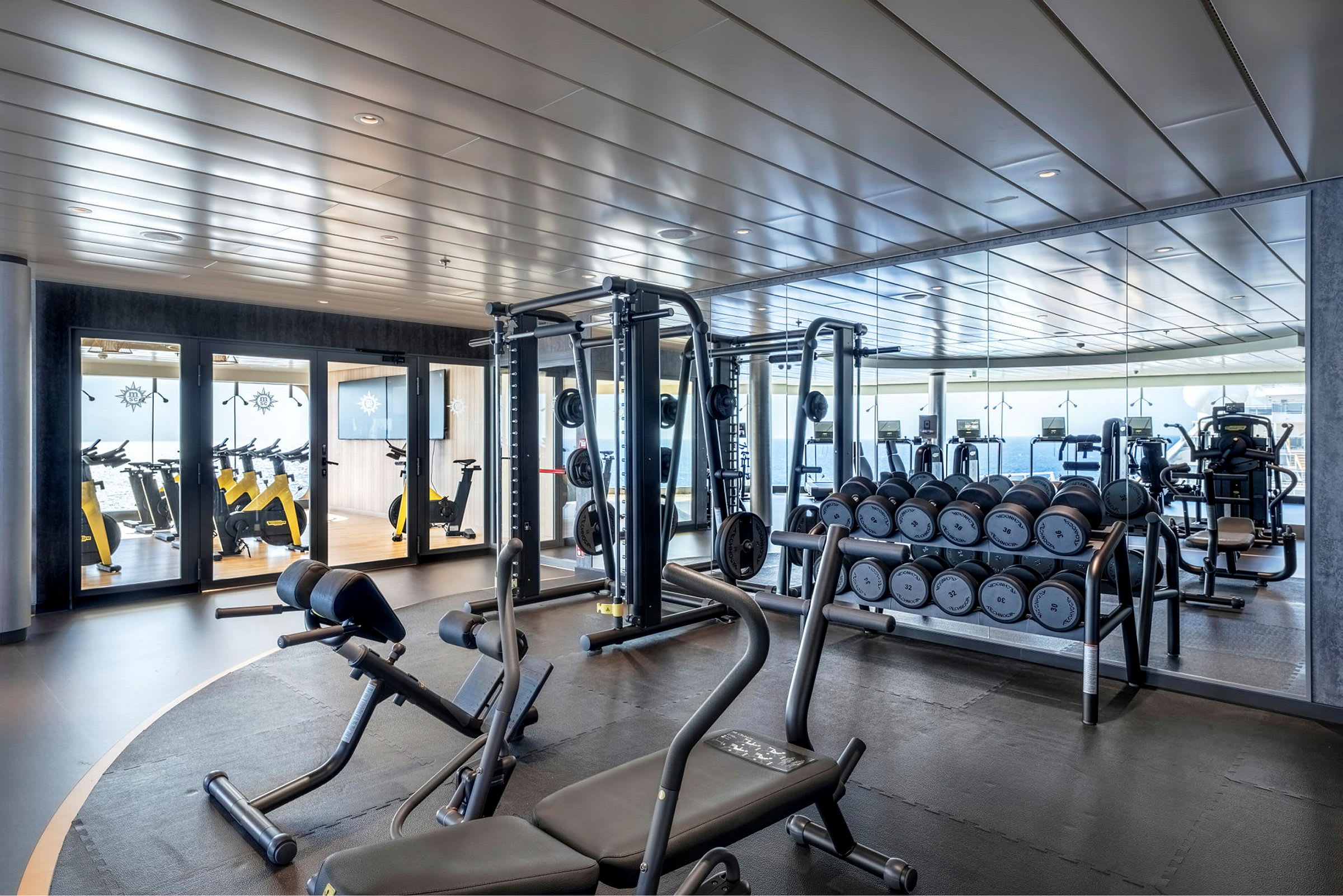 Billede af et fitnesscenter med træningsudstyr, håndvægte og spejle. (AI-genereret tekst)