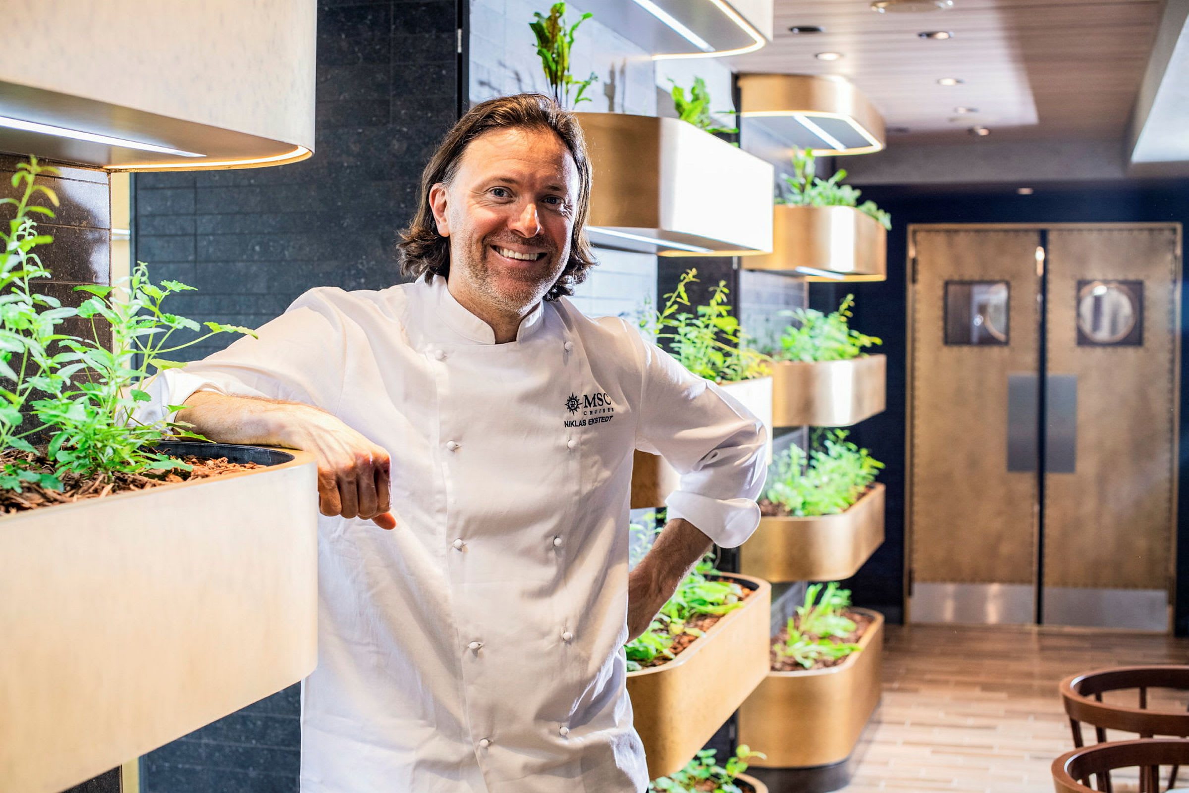 Kokken står ved siden af planteinstallationer i en restaurantmiljø. (AI-genereret tekst)