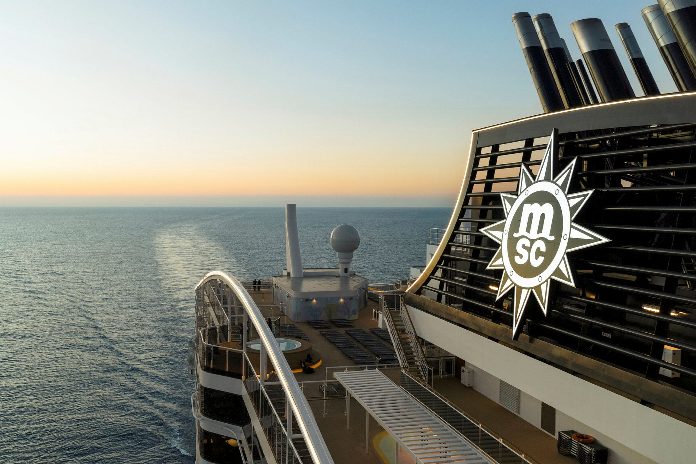 Solterrasse på et krydstogtskib med MSC-logo, havet og solnedgang i baggrunden. (AI-genereret tekst)