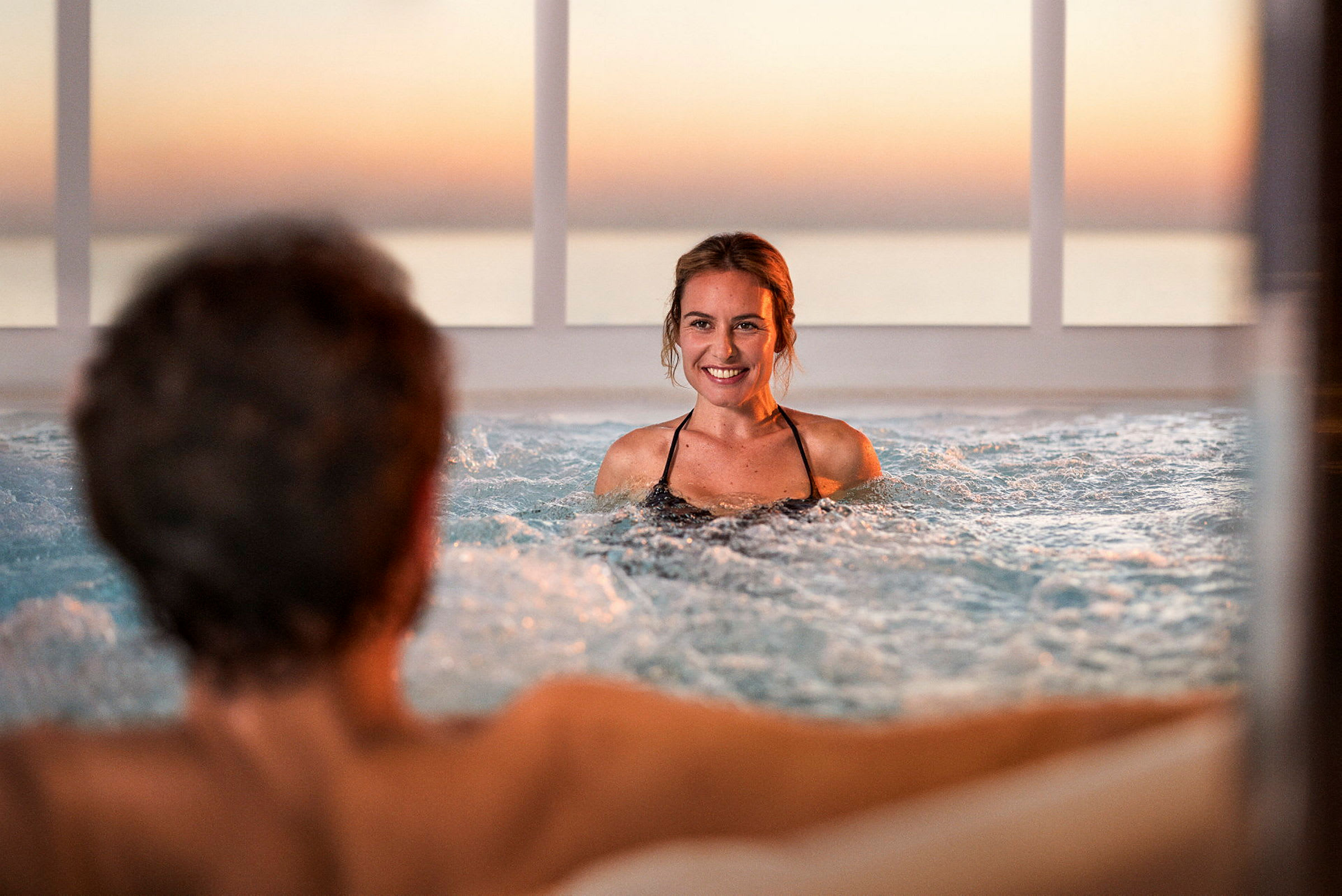 Personer nyder en jacuzzi med en solnedgang i baggrunden. (AI-genereret tekst)