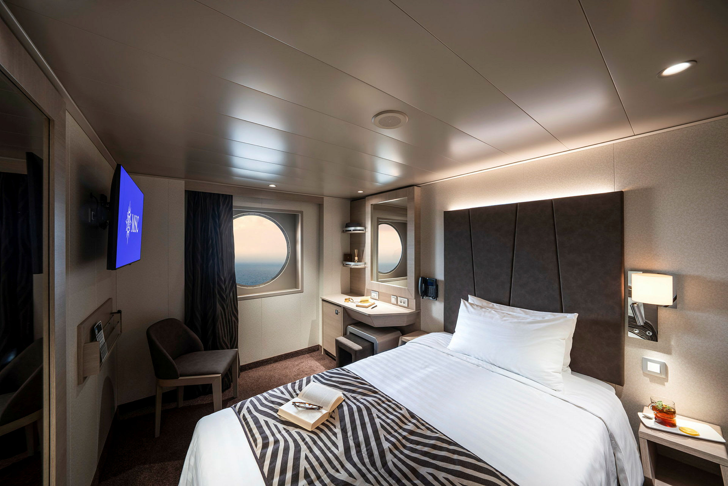 Et moderne hotelværelse med en seng, et rundt vindue og et fjernsyn. (AI-genereret tekst)
