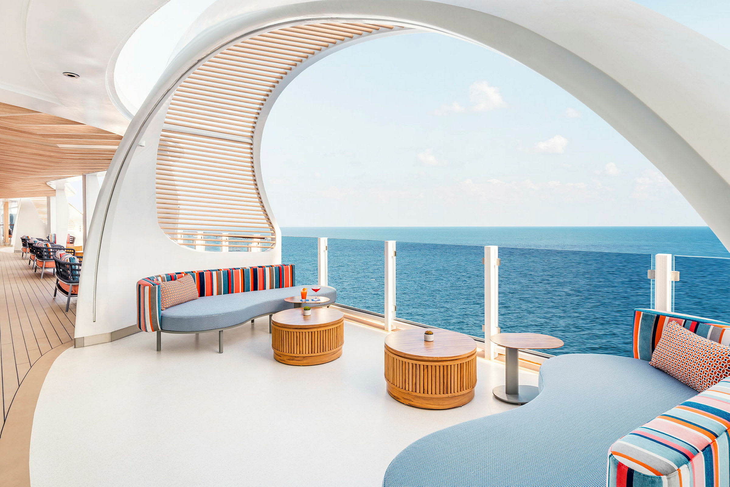 En moderne lounge med farverige sofaer, træborde og udsigt over havet. (AI-genereret tekst)