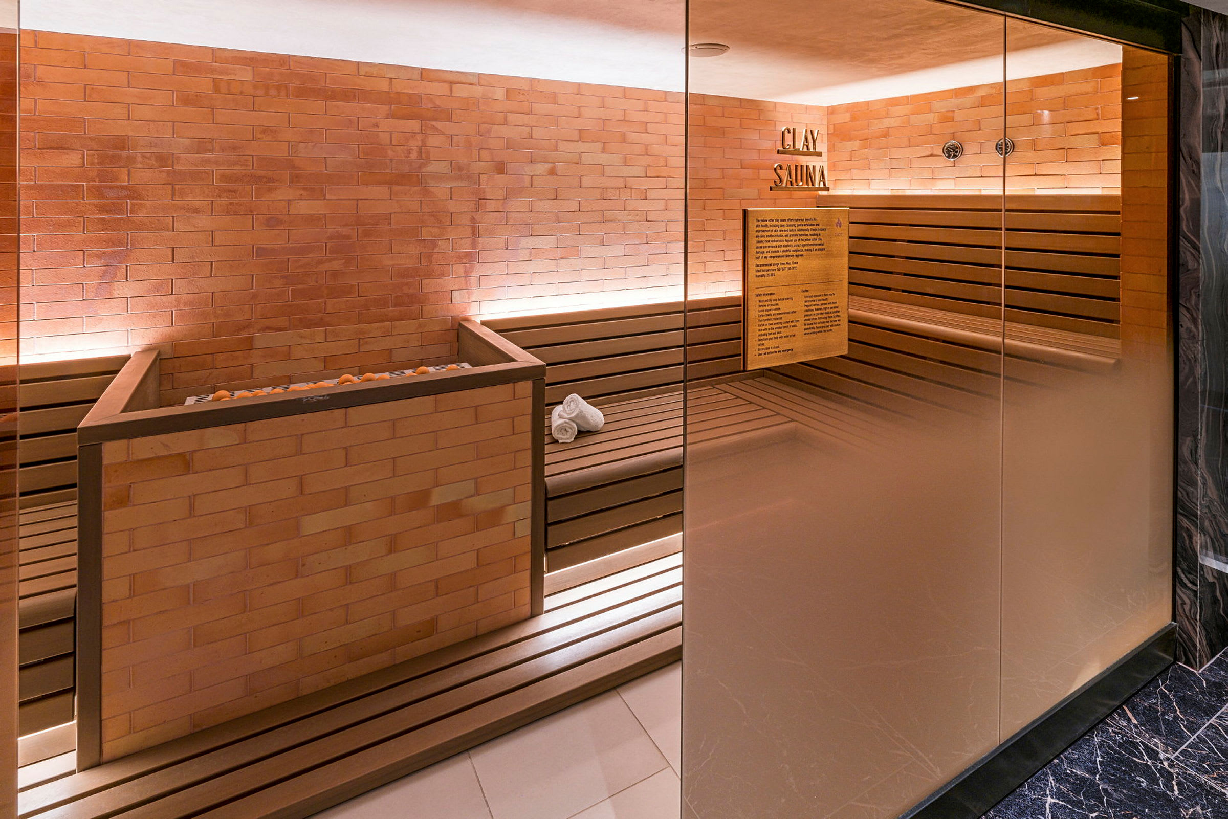 Billede af en indendørs sauna med murstensvægge, træbænke og glasvægge. (AI-genereret tekst)