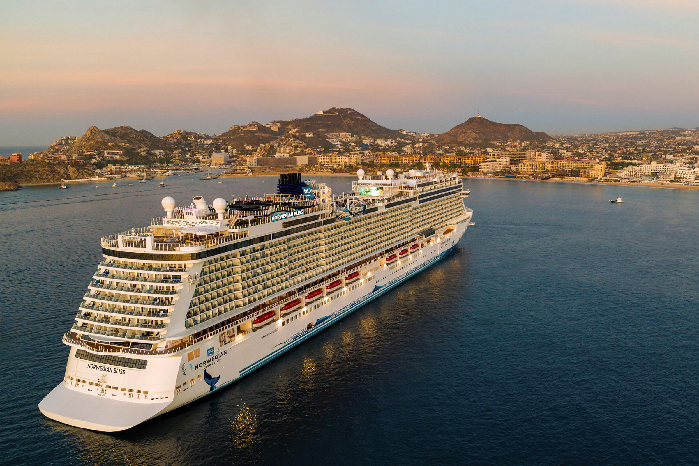 Et billede af krydstogtskibet Norwegian Bliss ved en kystby under solnedgangen. (AI-genereret tekst)